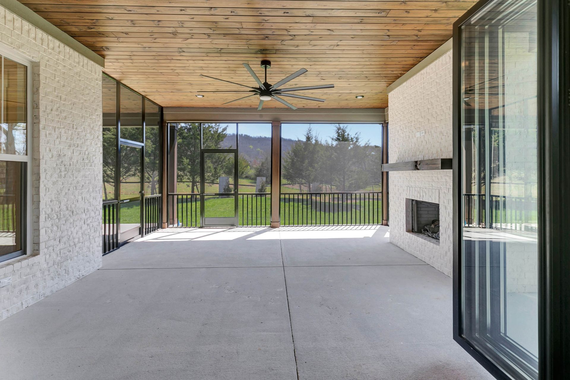 An empty screened in porch with a fireplace and a ceiling fan.