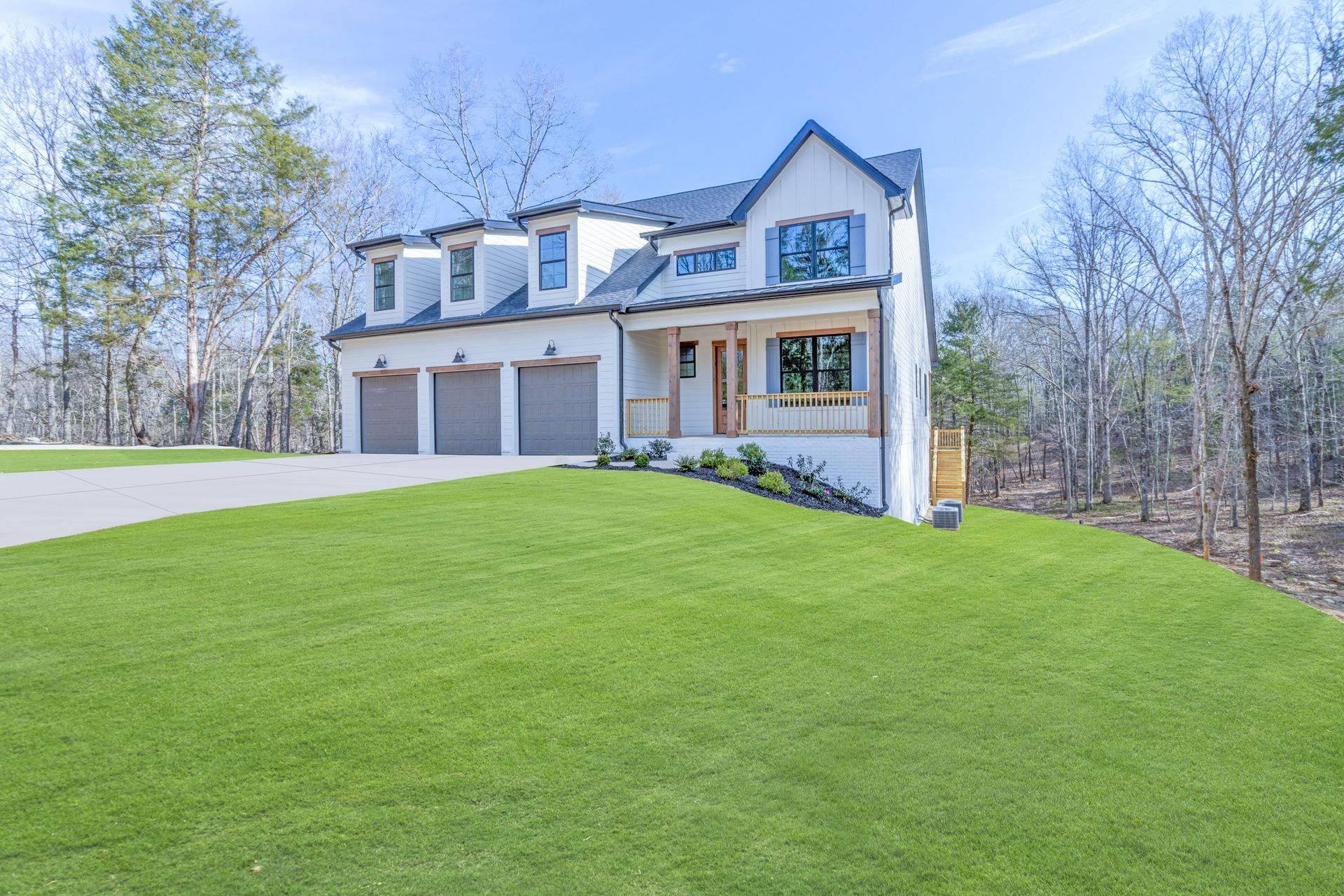 a large white house with three garages is sitting on top of a lush green hill .