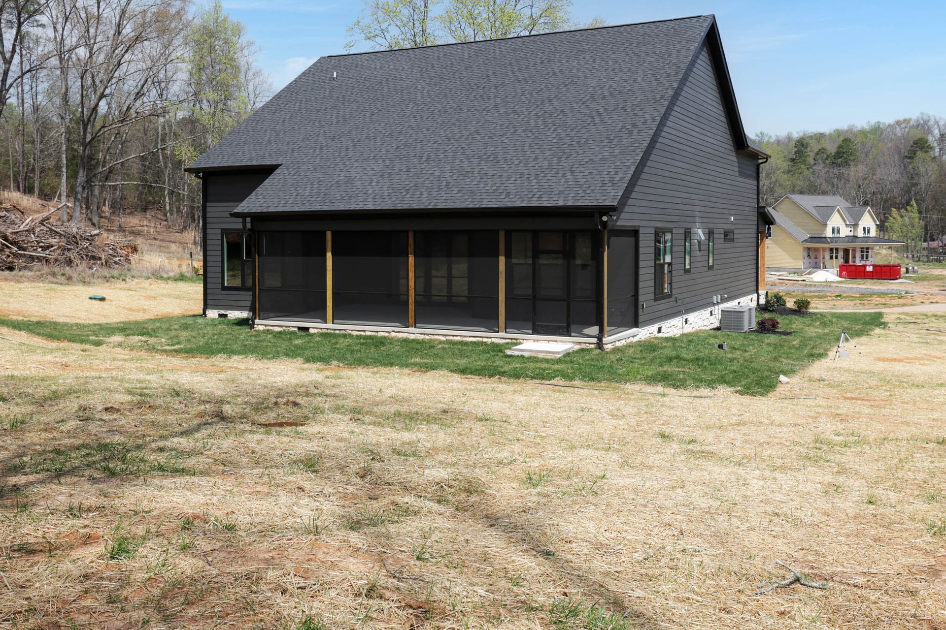 A black house with a porch is sitting in the middle of a grassy field.