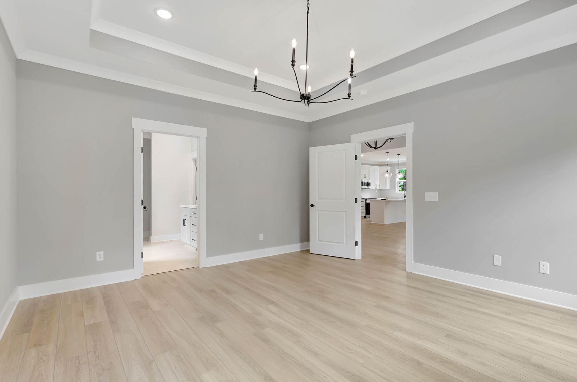 An empty living room with hardwood floors , gray walls and a chandelier.