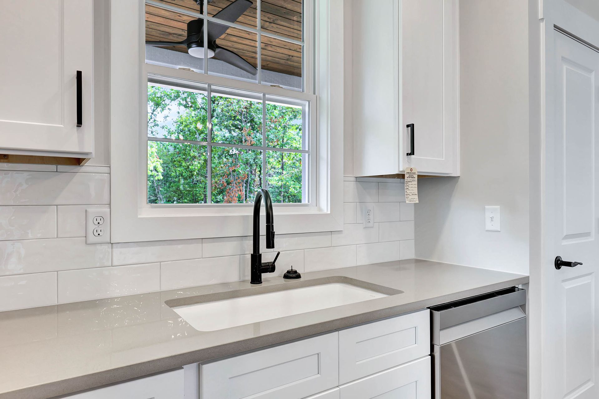 A kitchen with white cabinets , a sink , and a window.