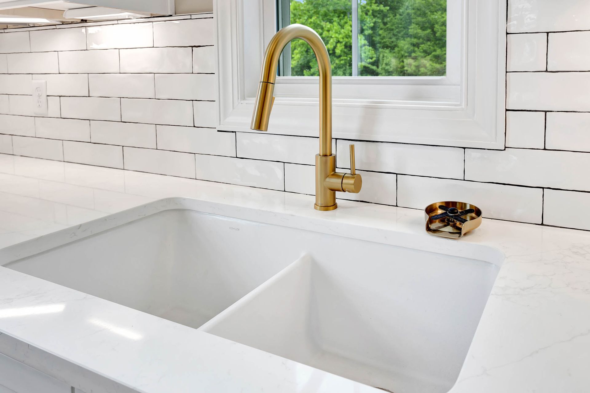 A kitchen sink with a gold faucet and white tiles.
