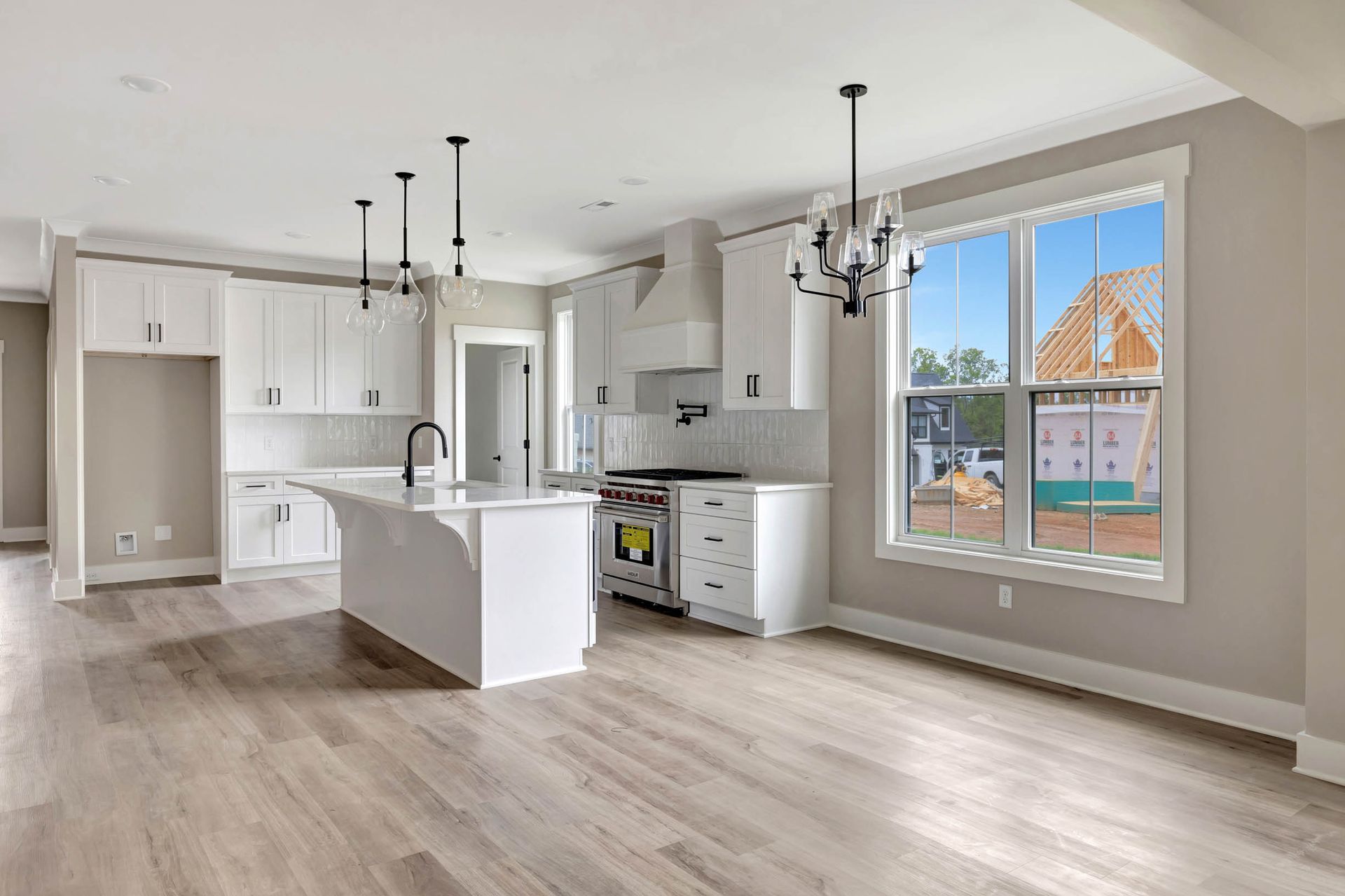 An empty kitchen with white cabinets and hardwood floors in a new home.