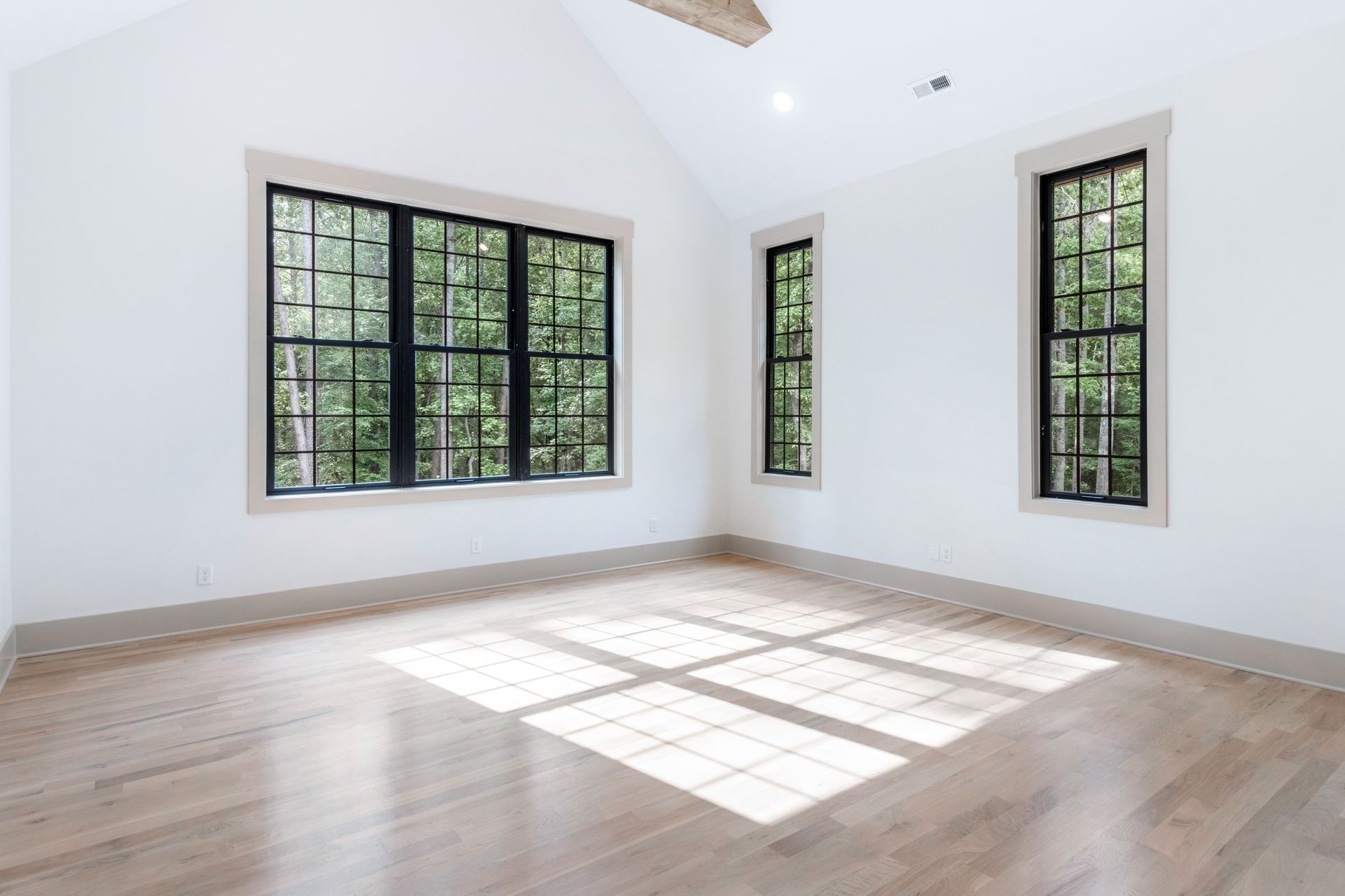 an empty room with hardwood floors and three windows .