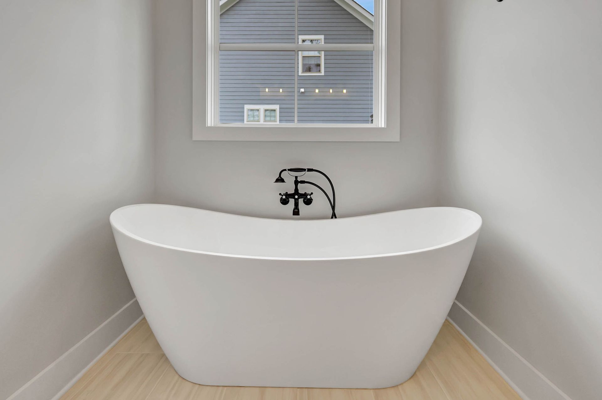 A white bathtub is sitting in a corner of a bathroom next to a window.