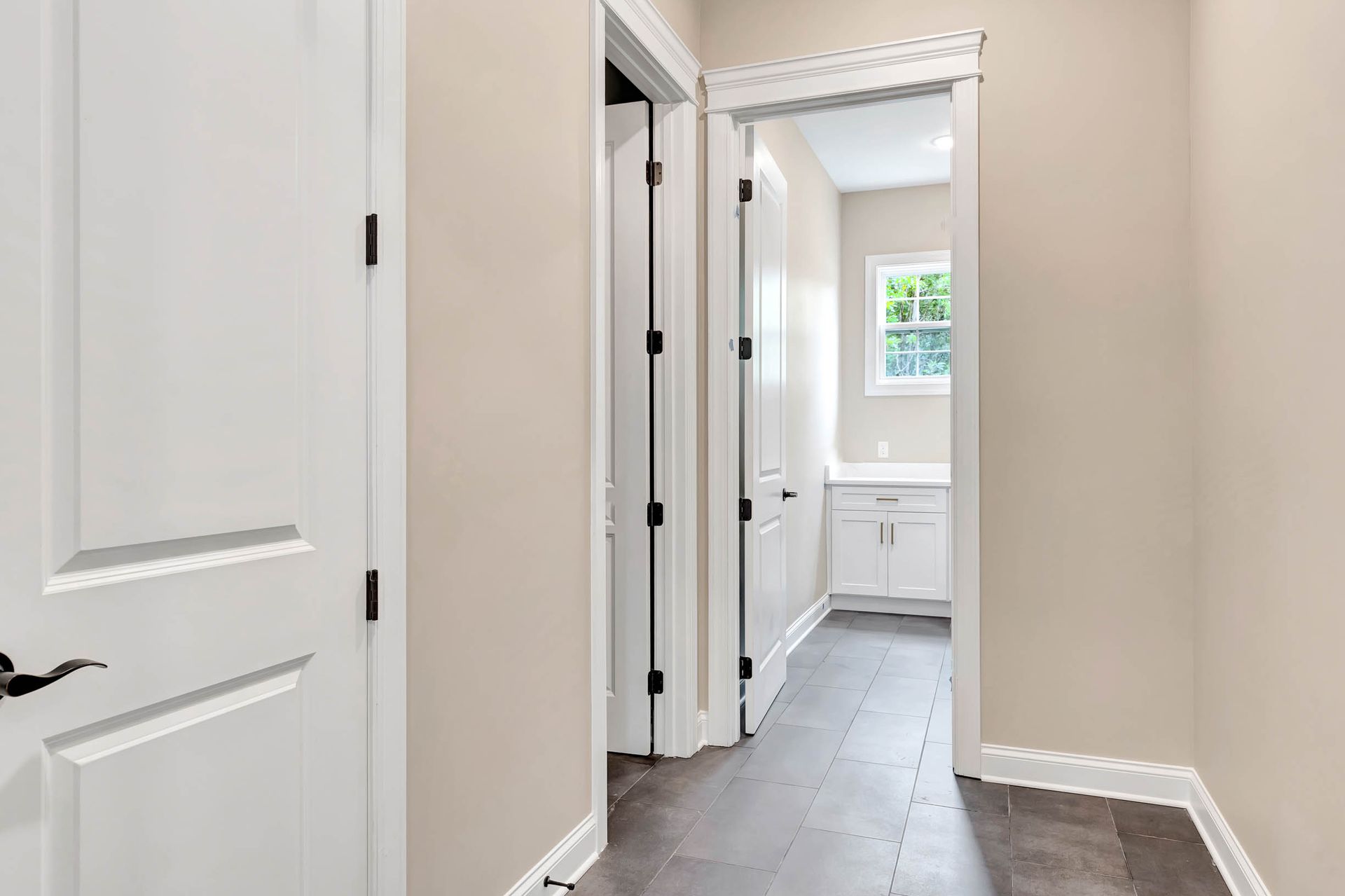 A hallway with white doors leading to a bathroom and a window.