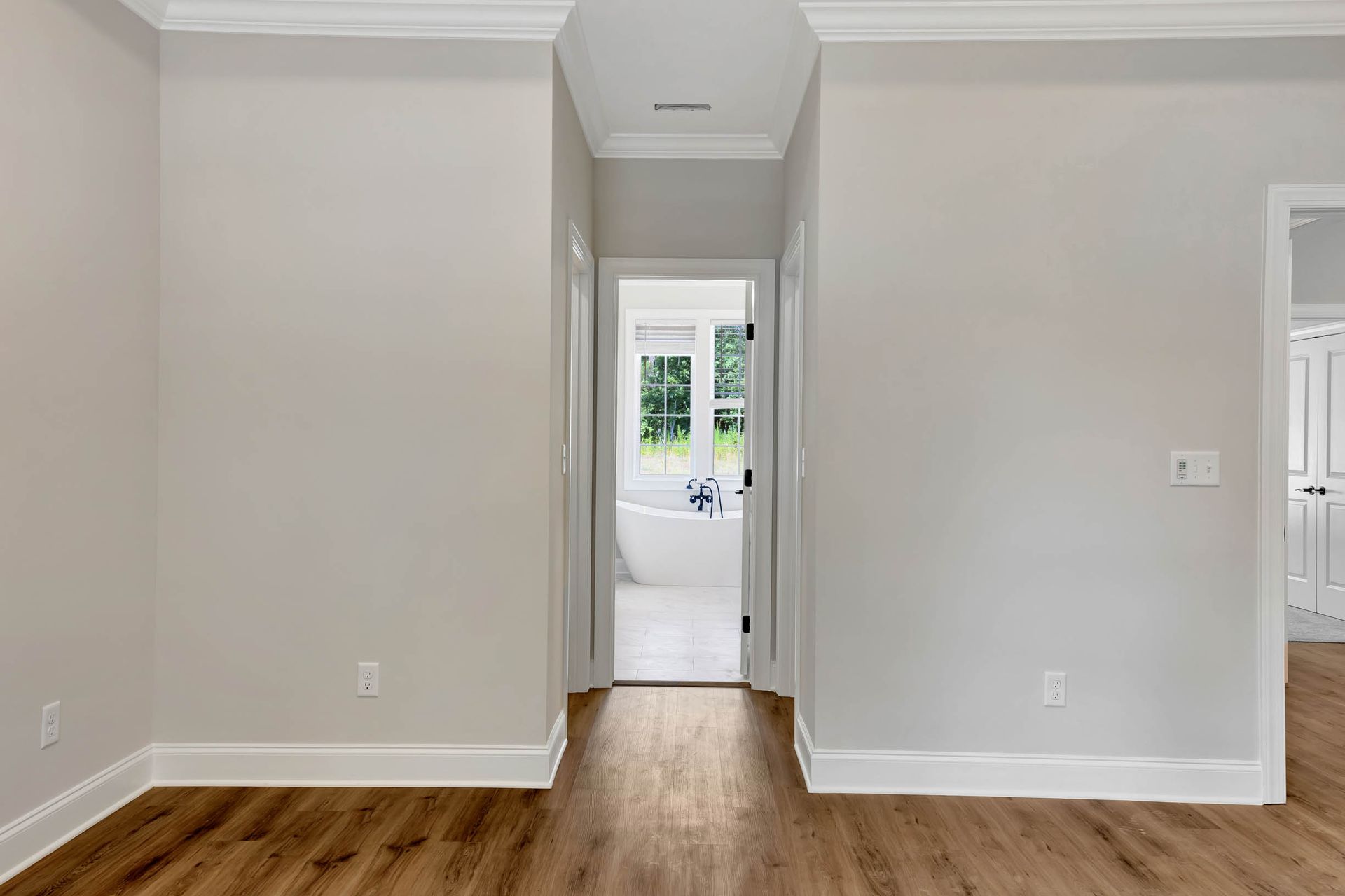 An empty room with hardwood floors and a bathroom in the background.