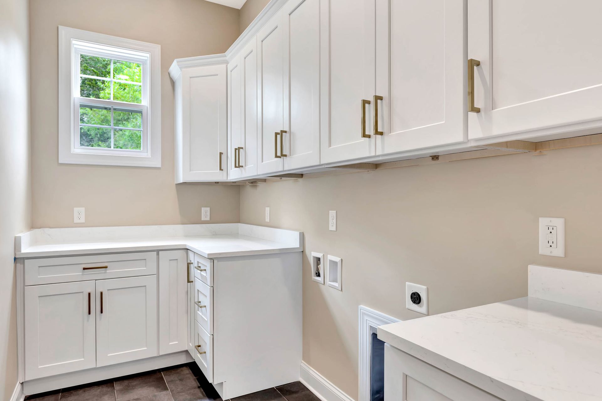 A laundry room with white cabinets , a washer and dryer , and a window.