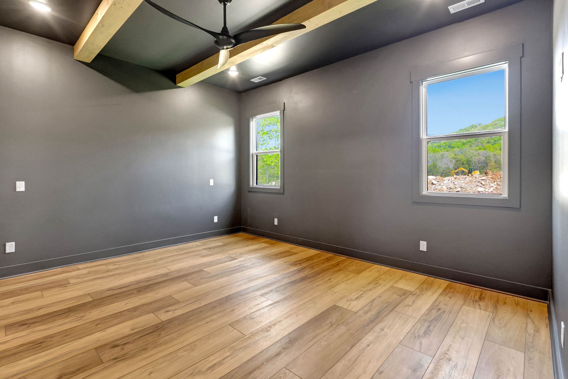 An empty room with a ceiling fan and two windows.
