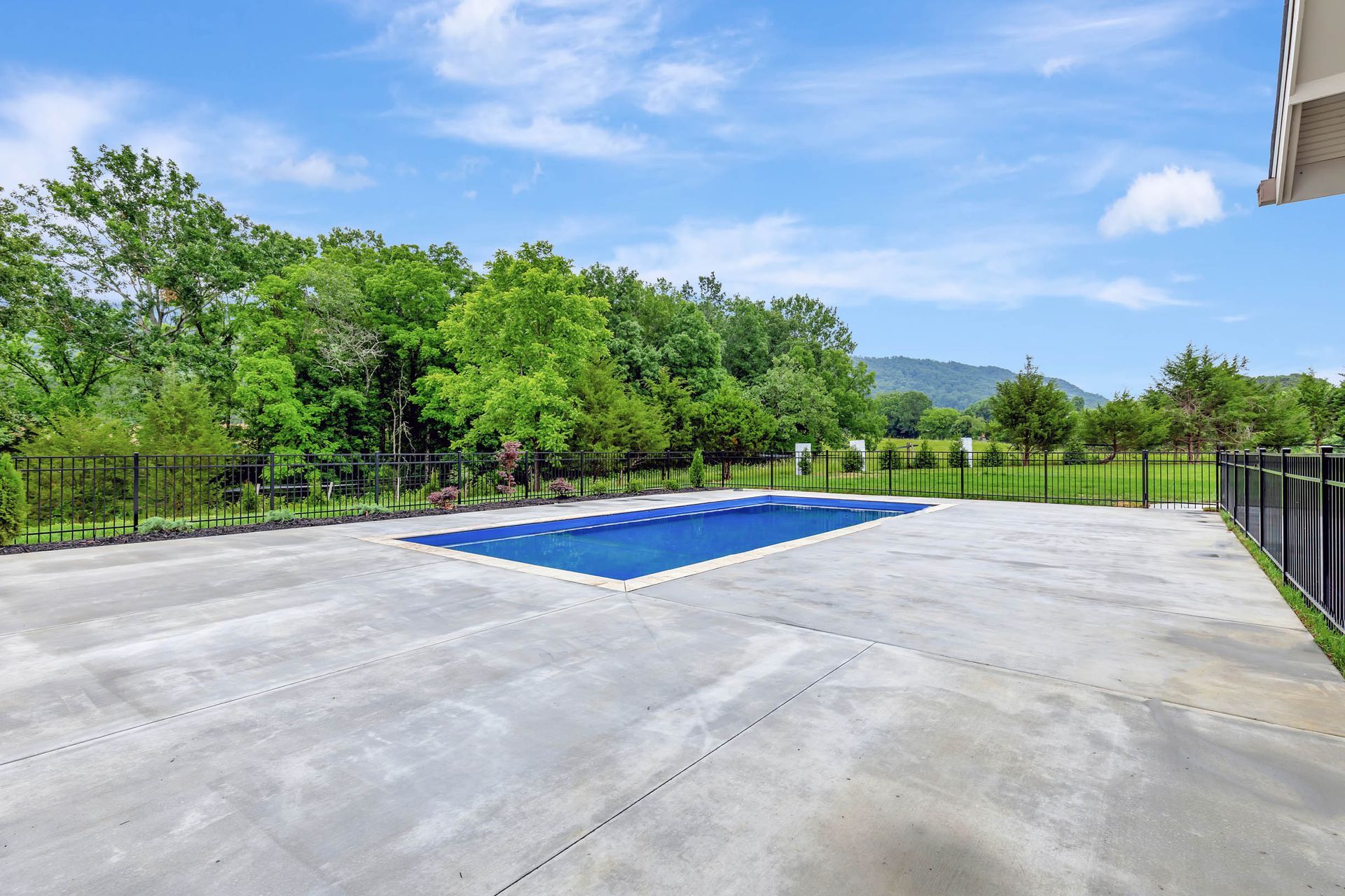 A large swimming pool is surrounded by trees and a fence.