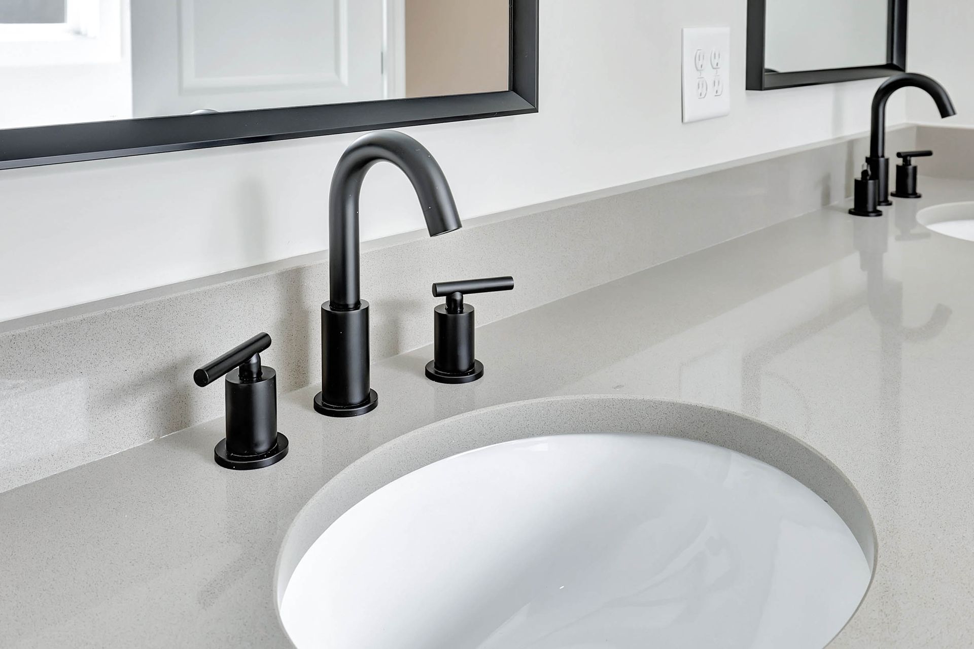 A bathroom sink with two black faucets and two mirrors.