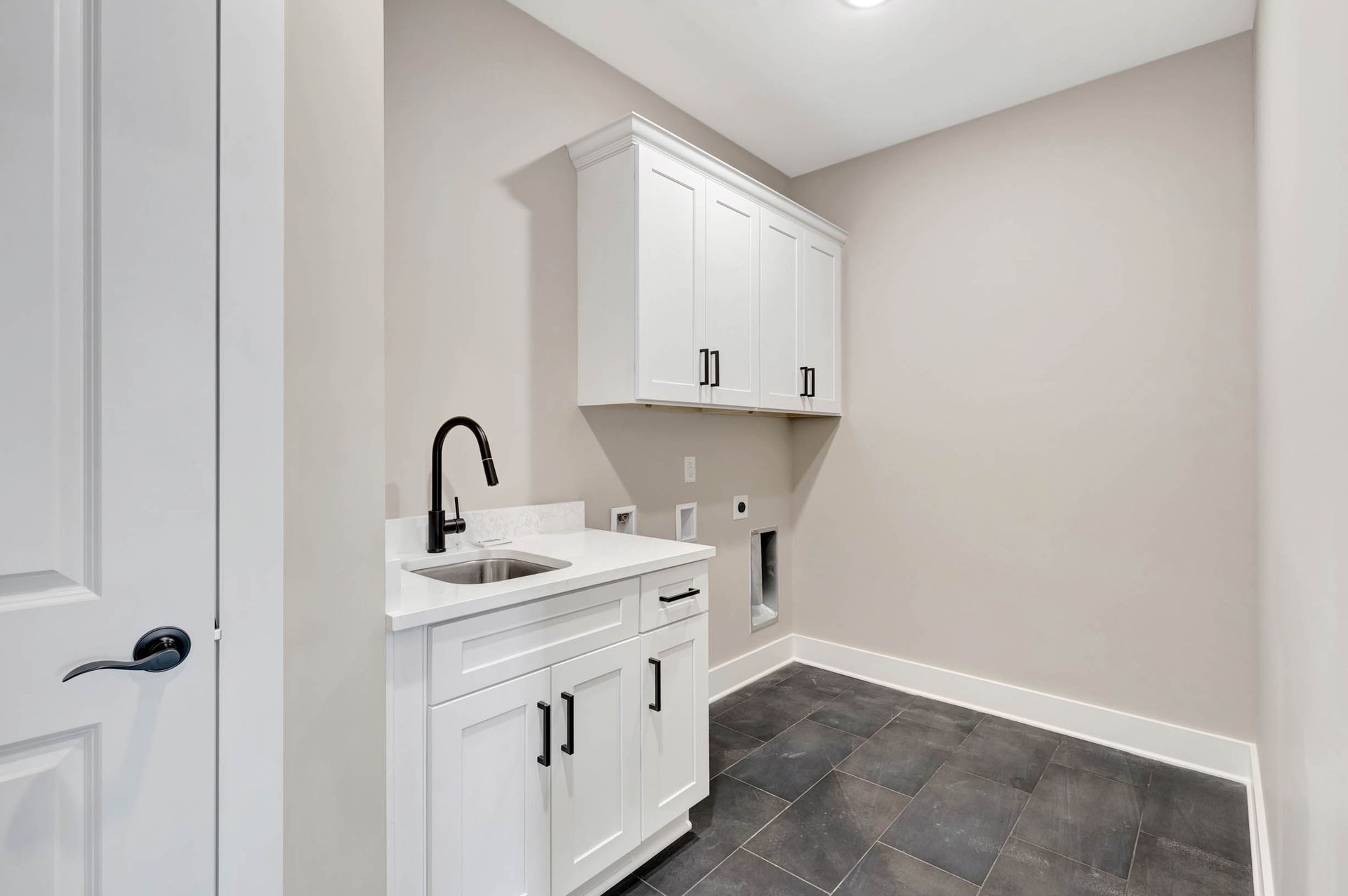 A laundry room with white cabinets and a sink.
