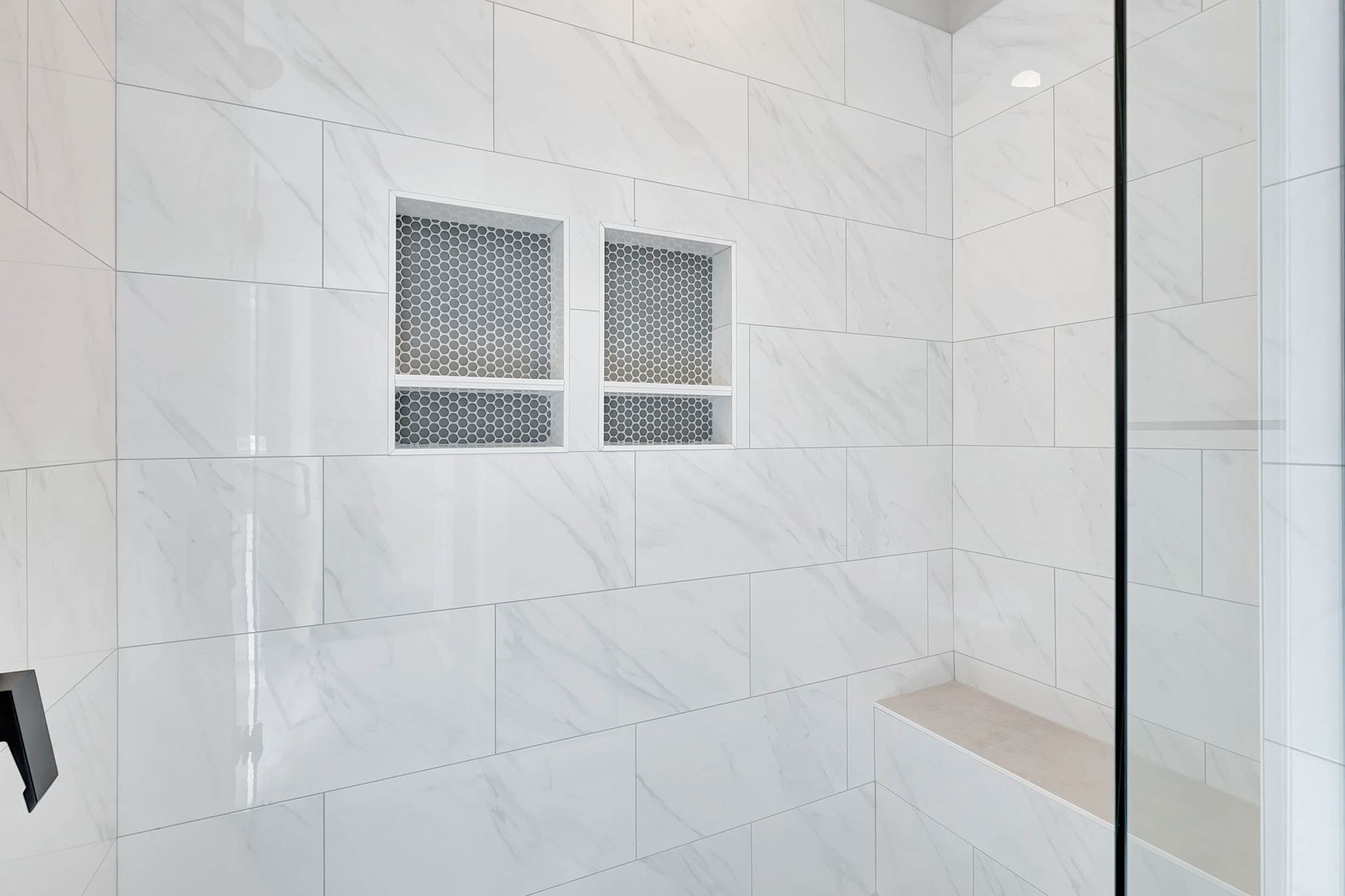A bathroom with white tiles and a walk in shower with a glass door.