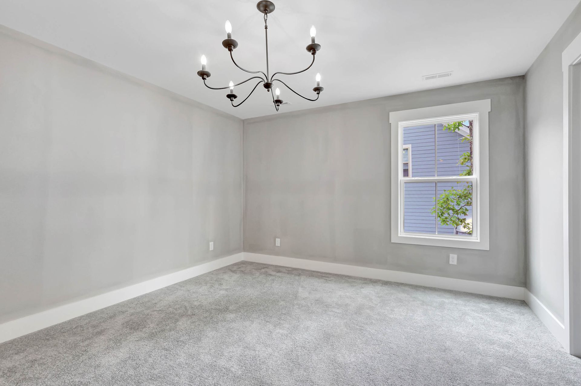 An empty room with a chandelier hanging from the ceiling and a window.