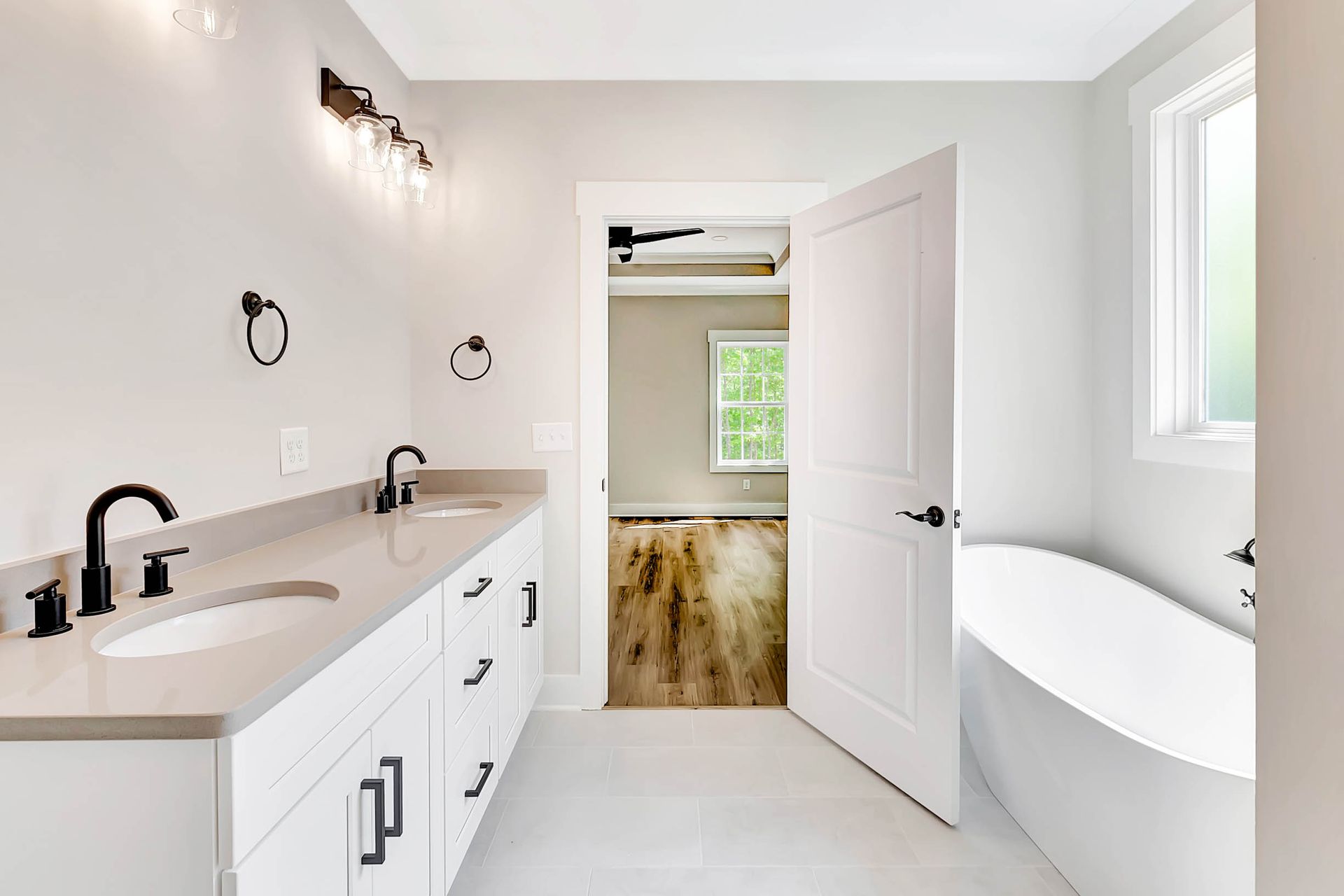 A bathroom with two sinks , a tub and a window.