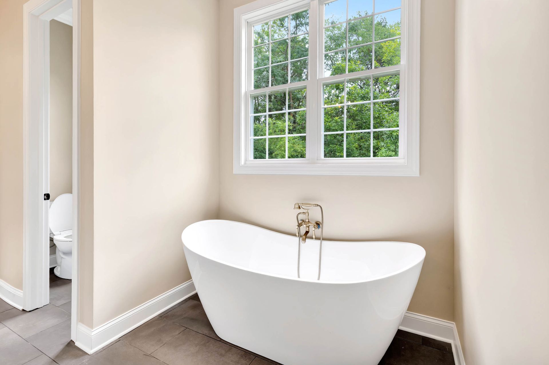 A bathroom with a tub , toilet , and window.