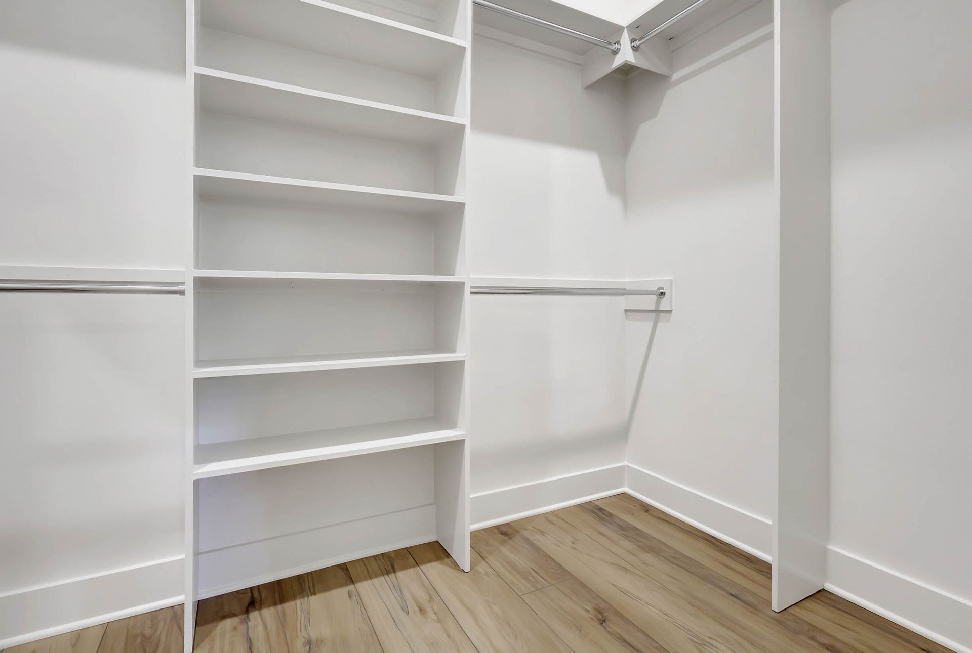 An empty walk in closet with white shelves and wooden floors.