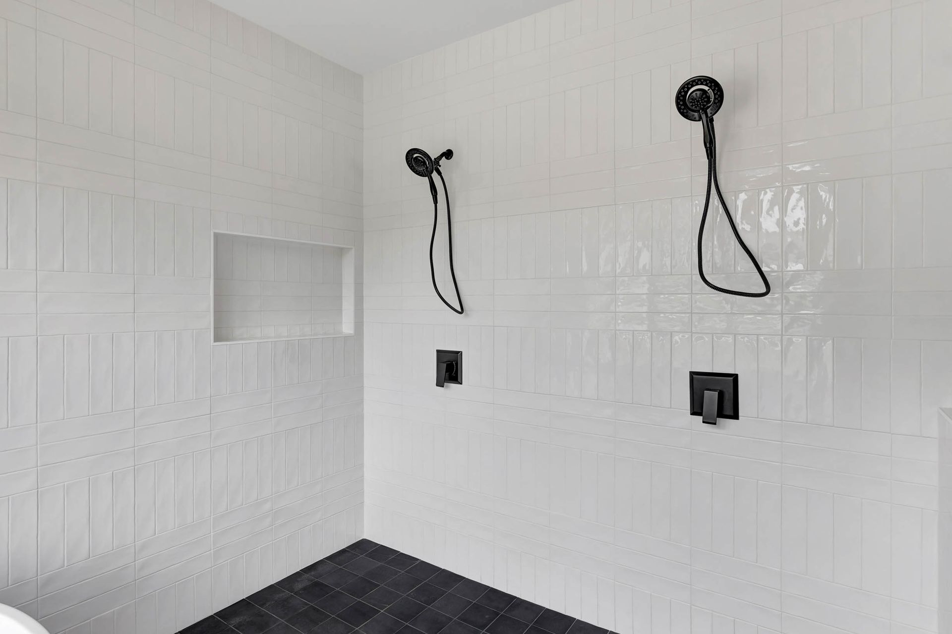 A bathroom with two shower heads and a black floor.