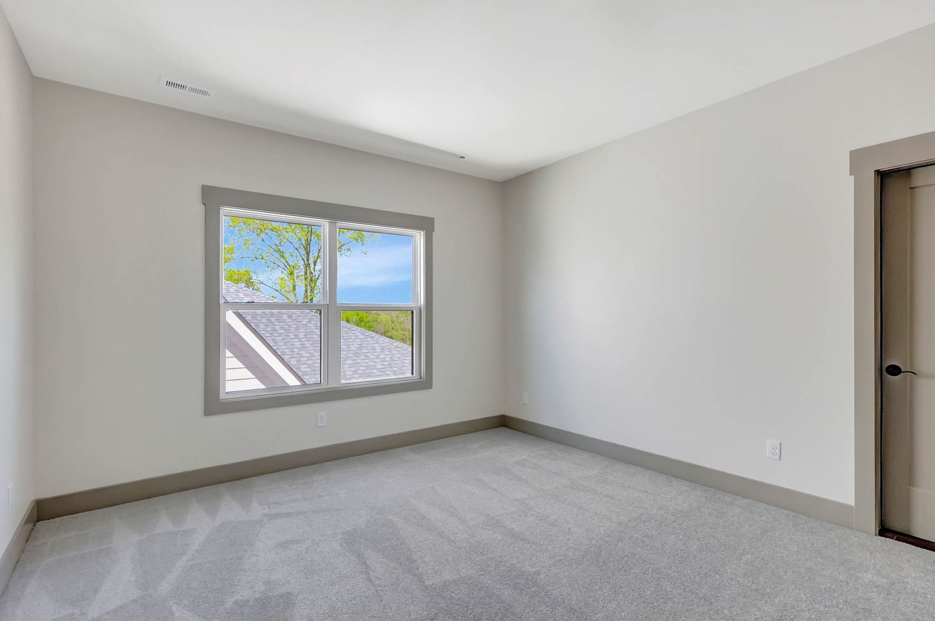 An empty bedroom with a window and a carpeted floor.