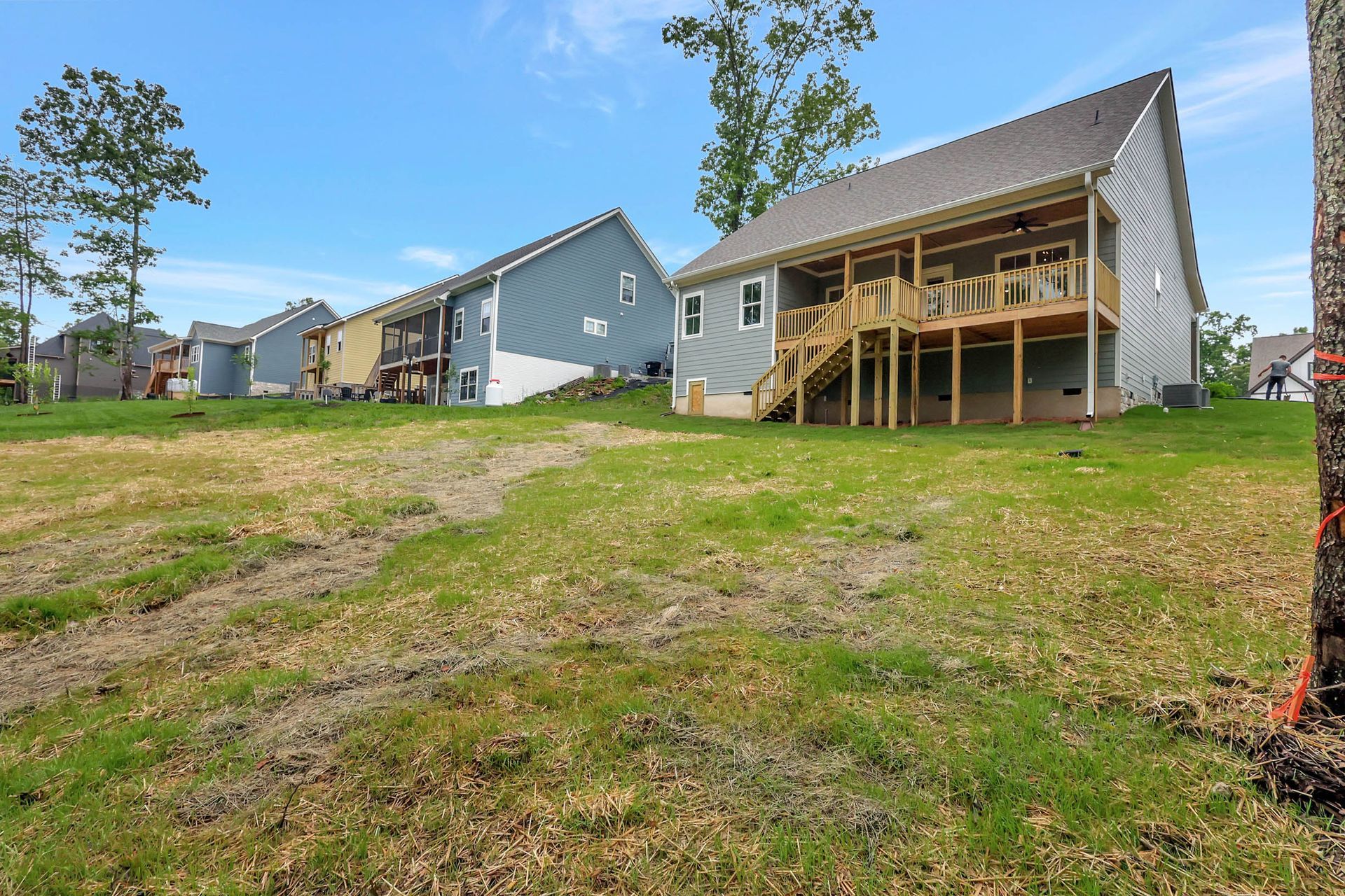 A house with a deck is sitting on top of a lush green field.