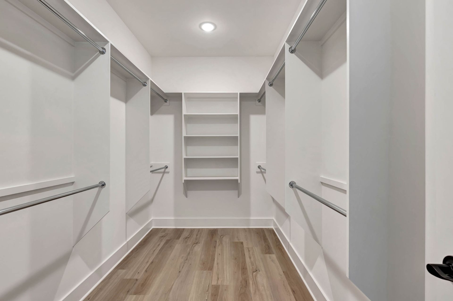 A walk in closet with wooden floors and white shelves.
