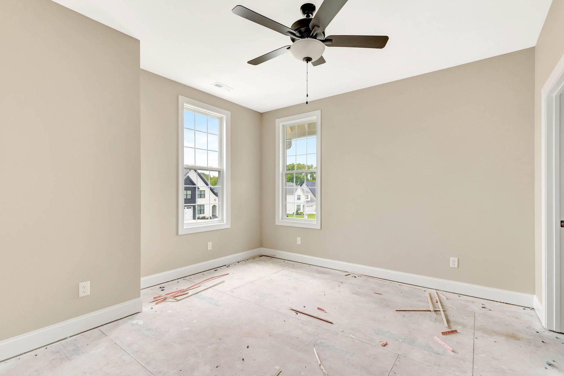 An empty room with a ceiling fan and two windows.