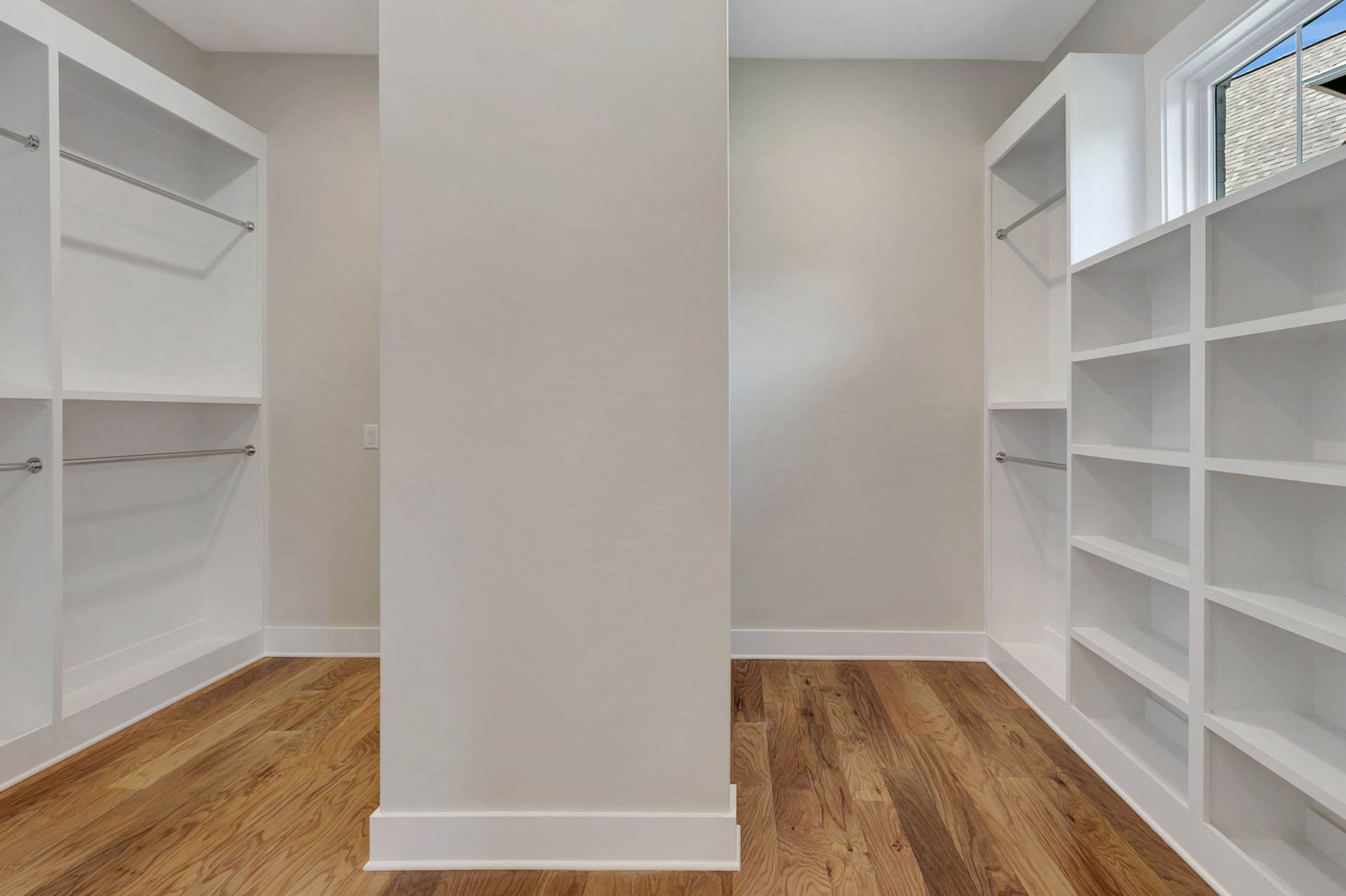 An empty walk in closet with hardwood floors and white shelves.