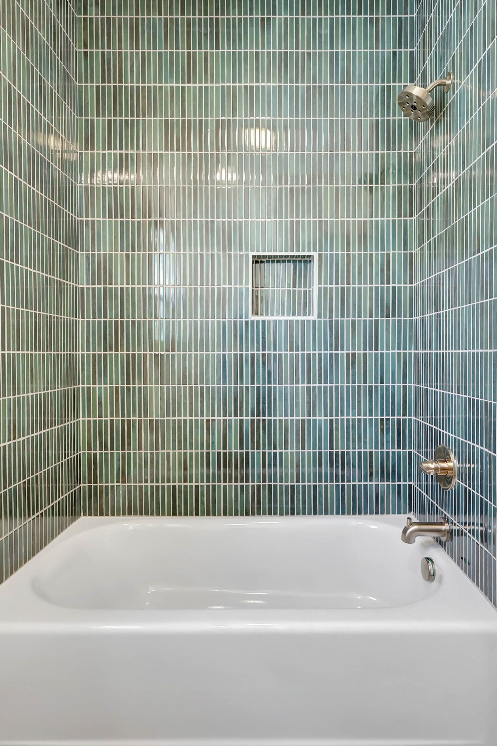 A bathtub in a bathroom with green tiles and a shower.