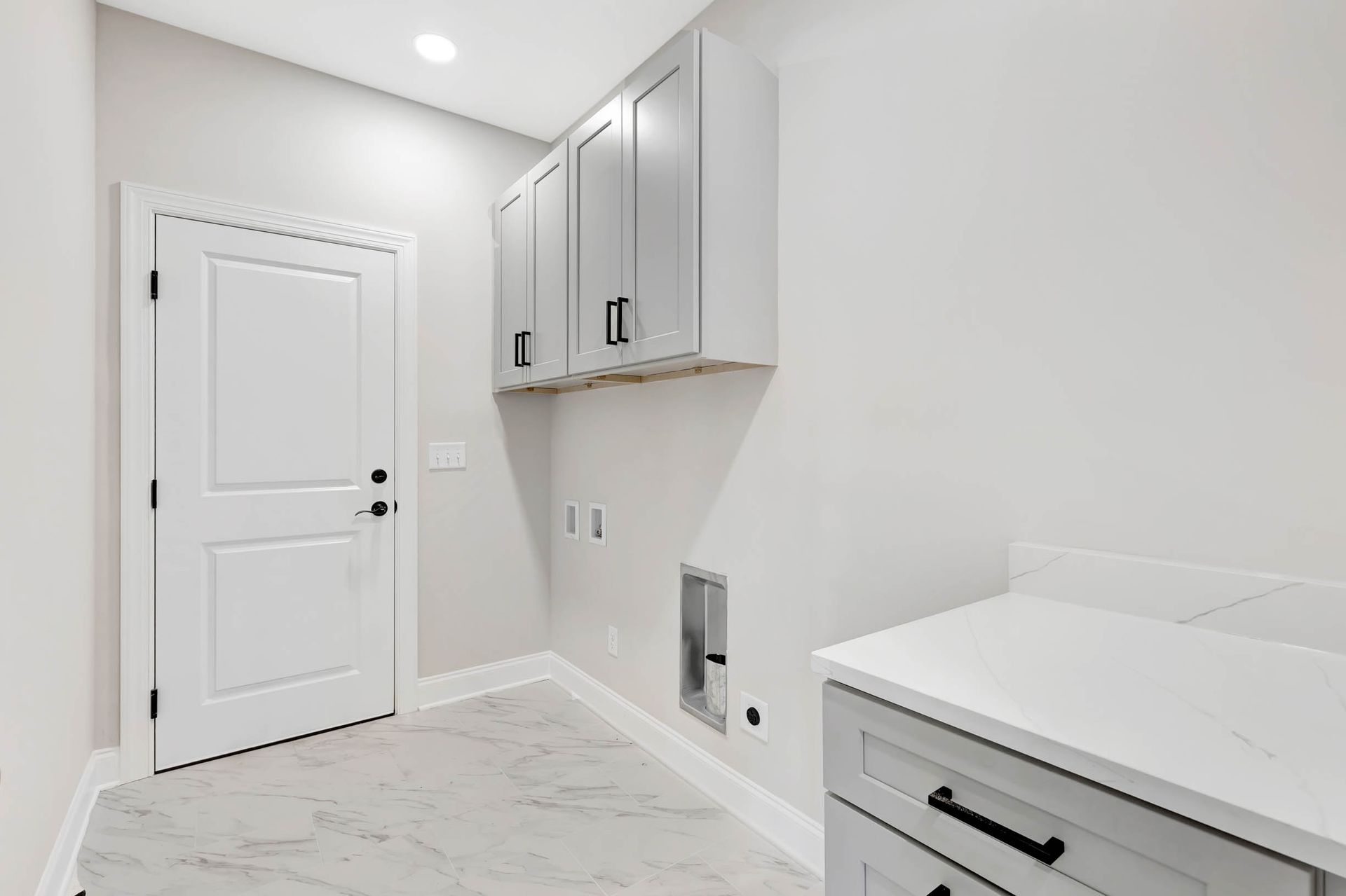 A laundry room with white cabinets , a sink , and a door.