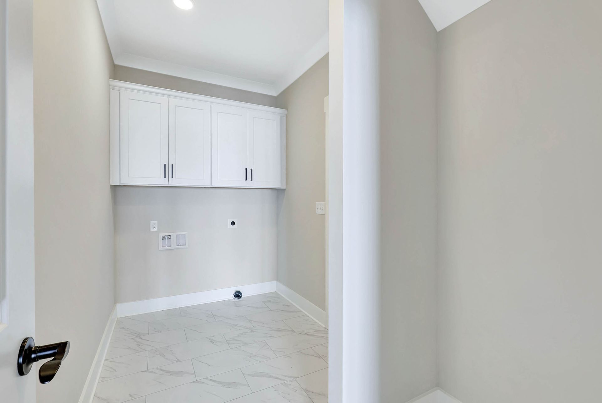 A laundry room with white cabinets and a marble floor.