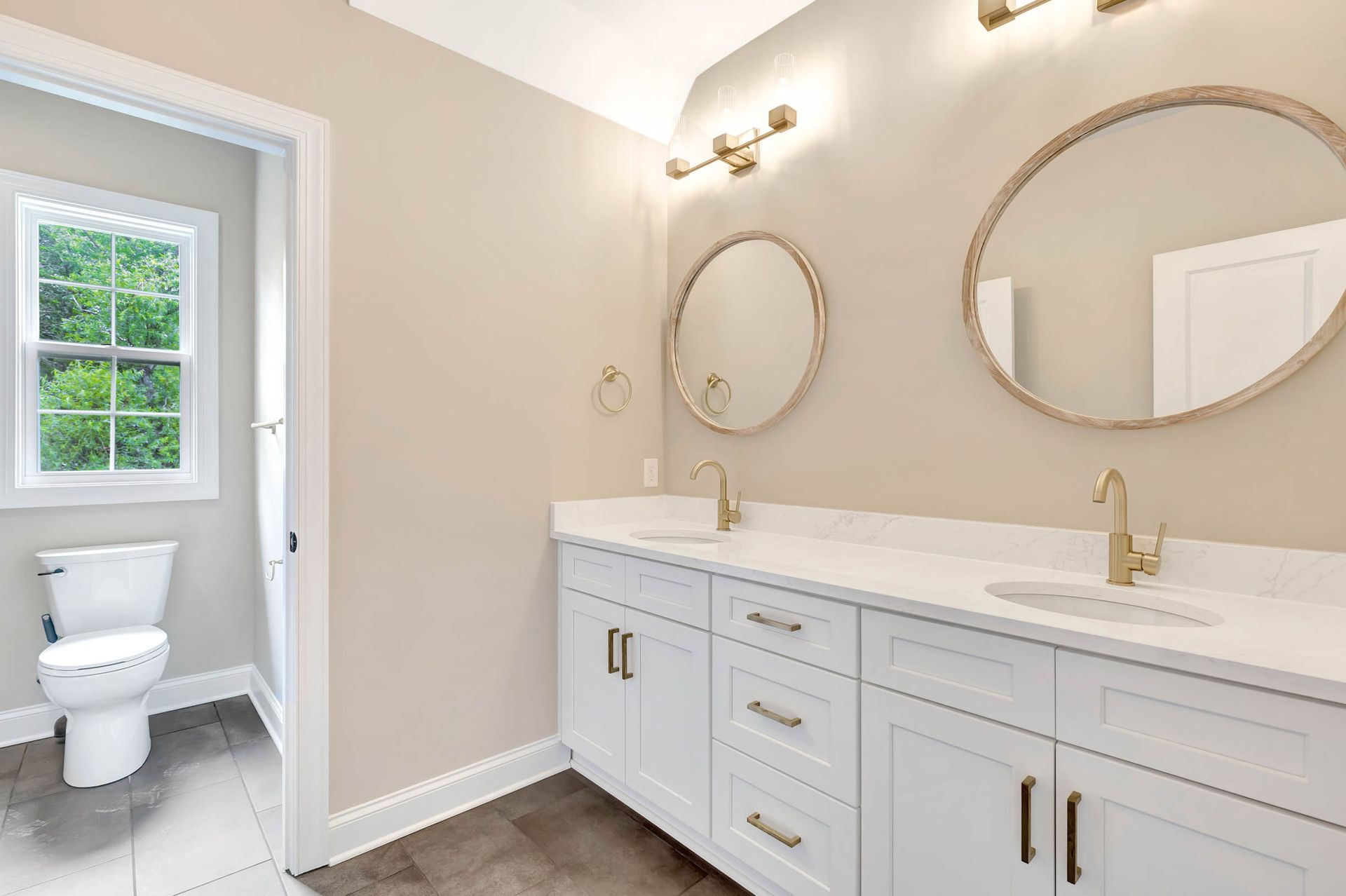 A bathroom with two sinks , two mirrors and a toilet.