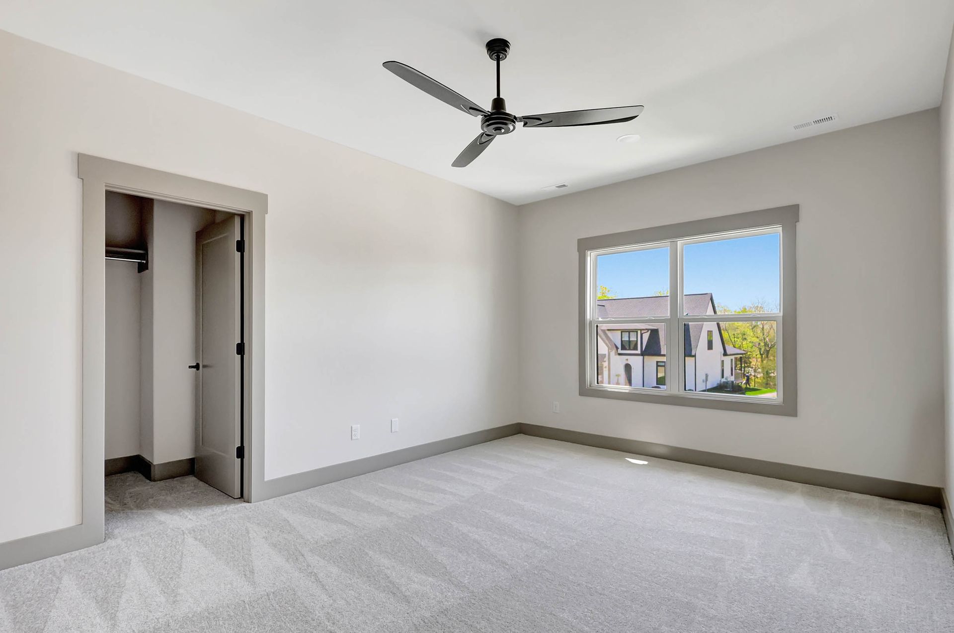 An empty bedroom with a ceiling fan and two windows.