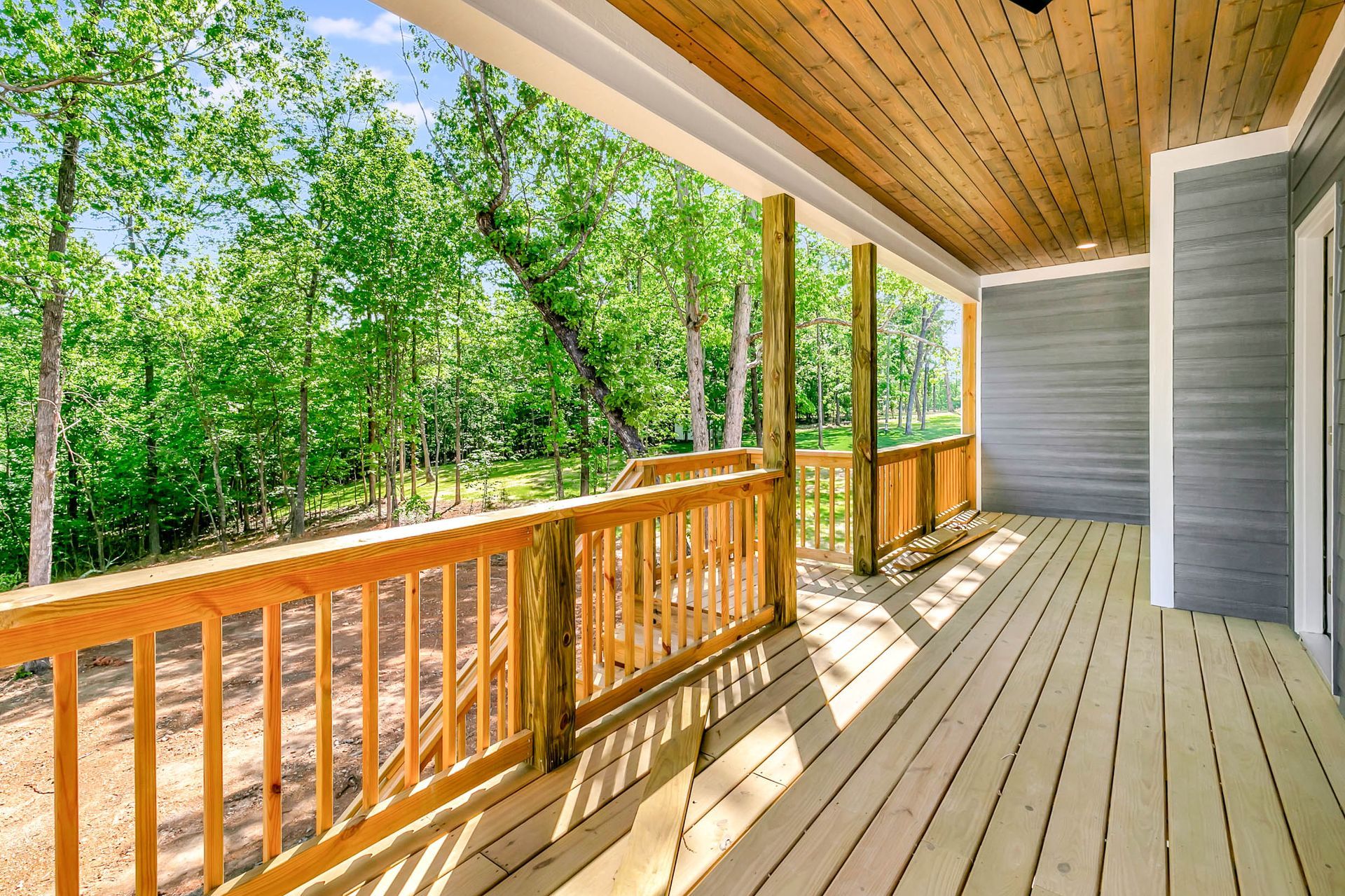 A large wooden deck with a wooden railing and trees in the background.