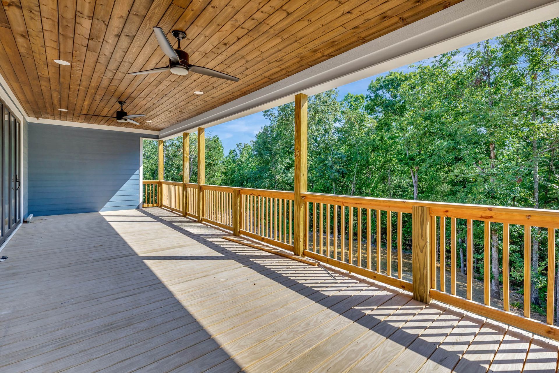 A large deck with a wooden railing and a ceiling fan.