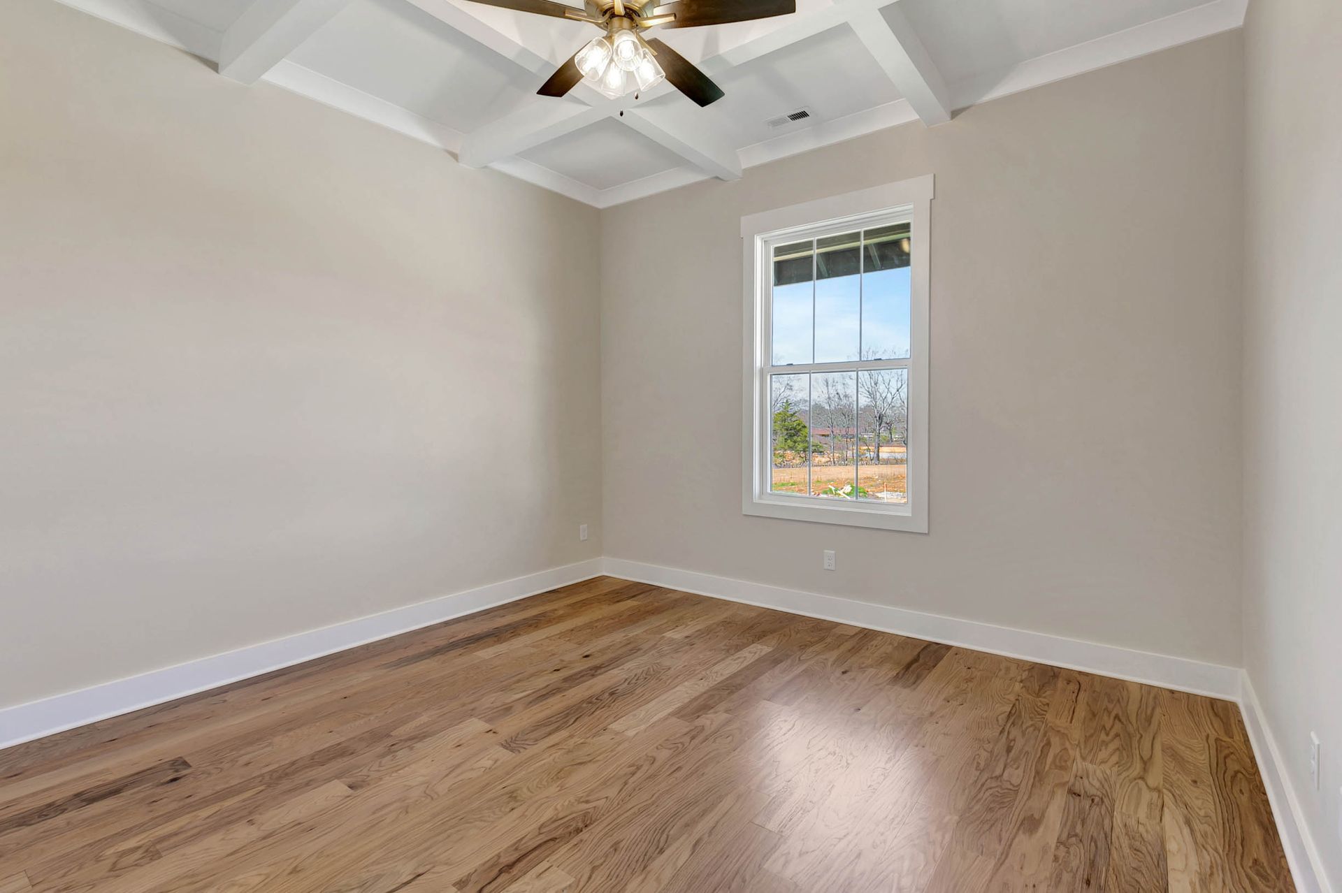 An empty room with hardwood floors and a ceiling fan.
