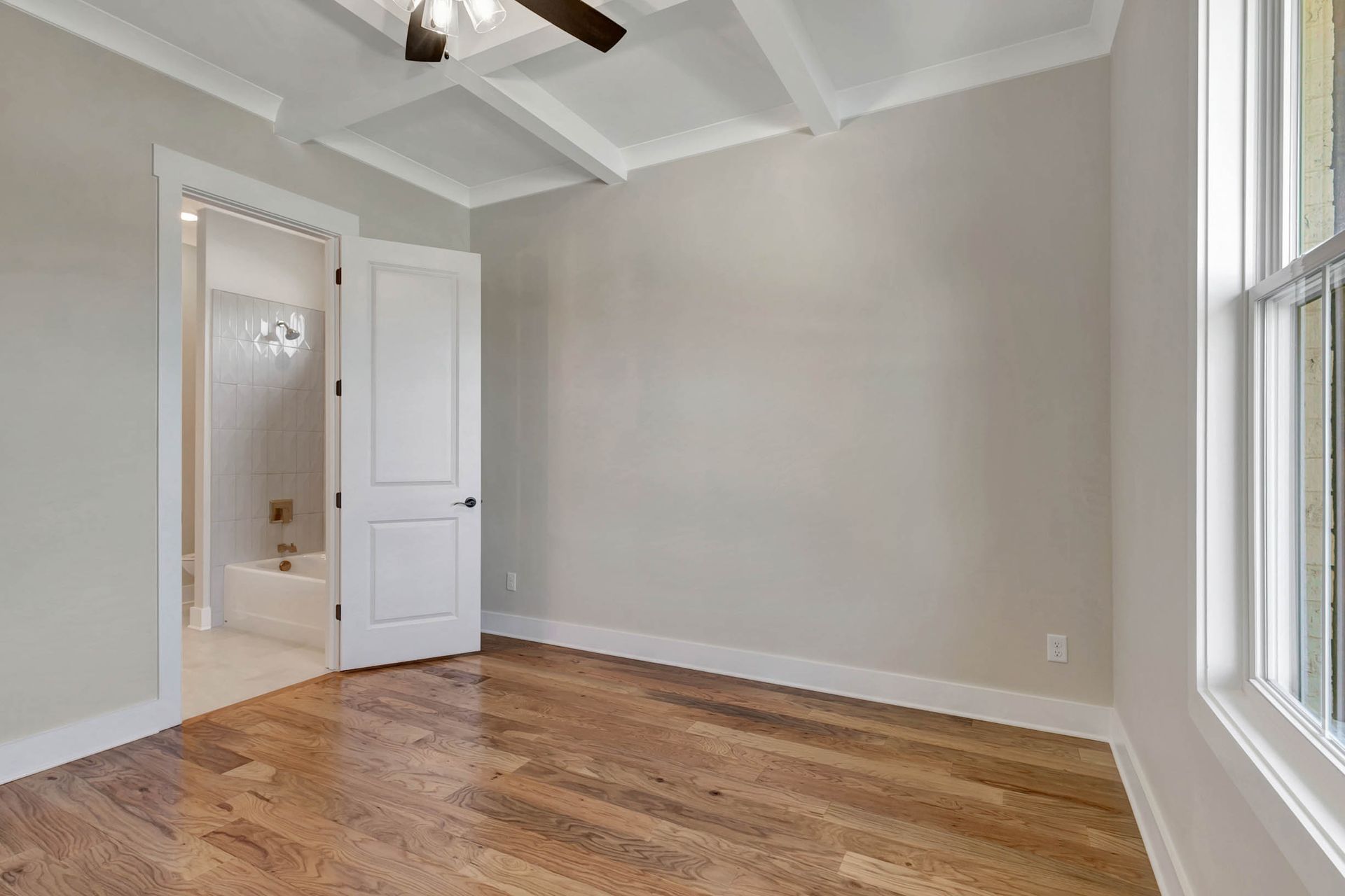 An empty bedroom with hardwood floors and a ceiling fan.