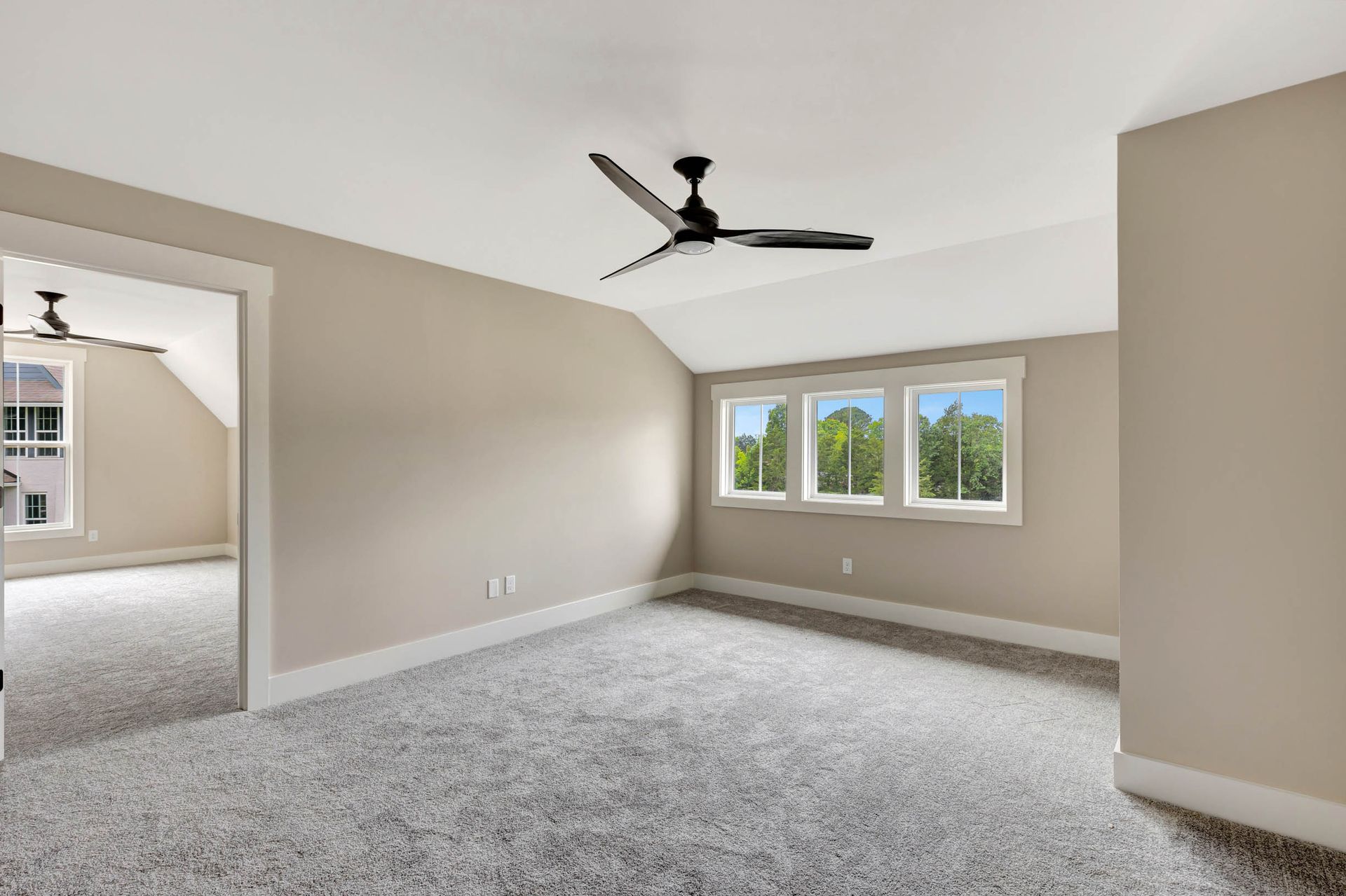 An empty bedroom with a ceiling fan and three windows.