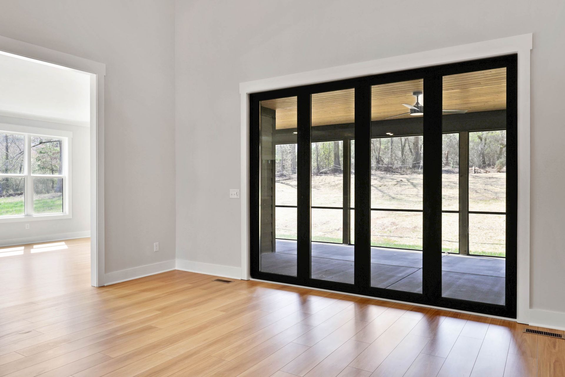 An empty room with hardwood floors and sliding glass doors leading to a screened in porch.