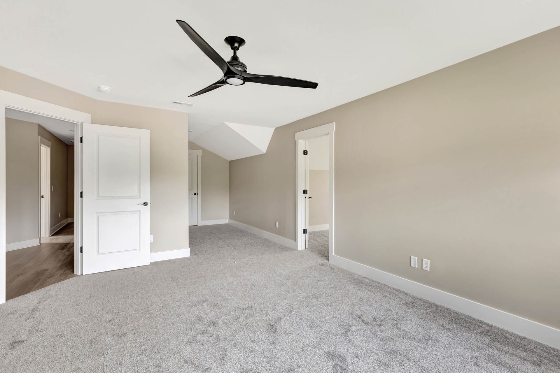 An empty bedroom with a ceiling fan and a gray carpet.