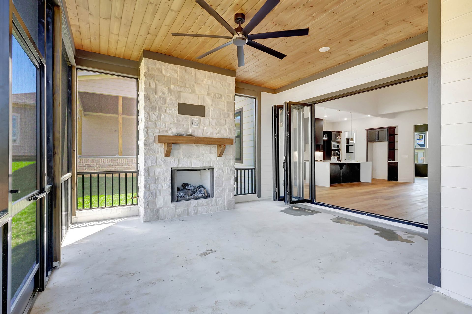 A screened in porch with a fireplace and ceiling fan.