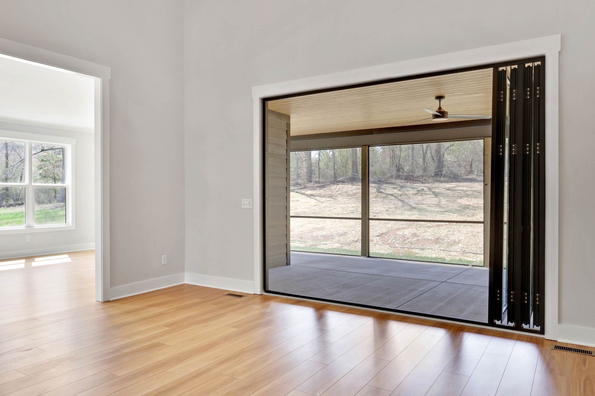 An empty room with hardwood floors and a screened in porch.