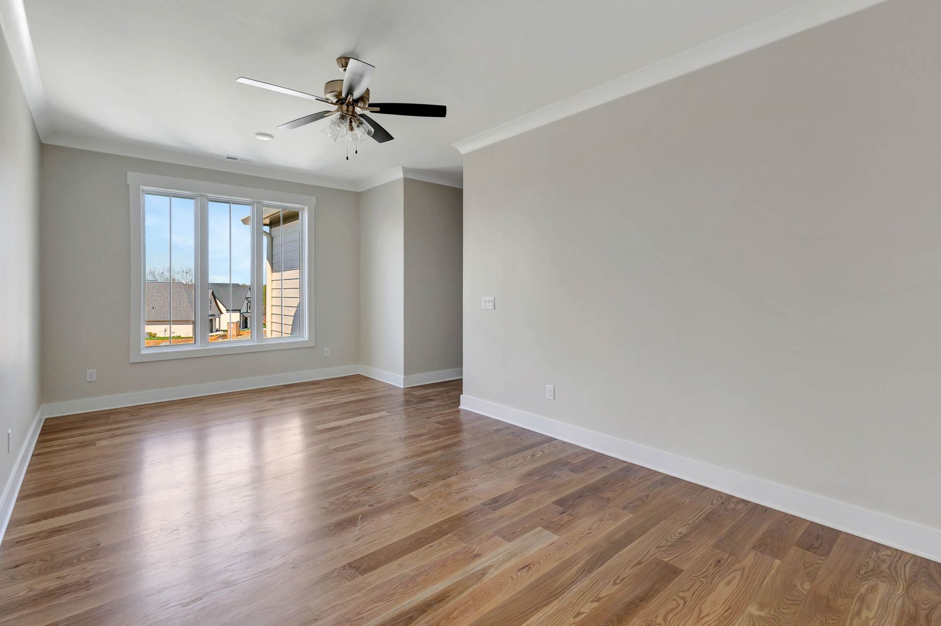 An empty living room with hardwood floors and a ceiling fan.