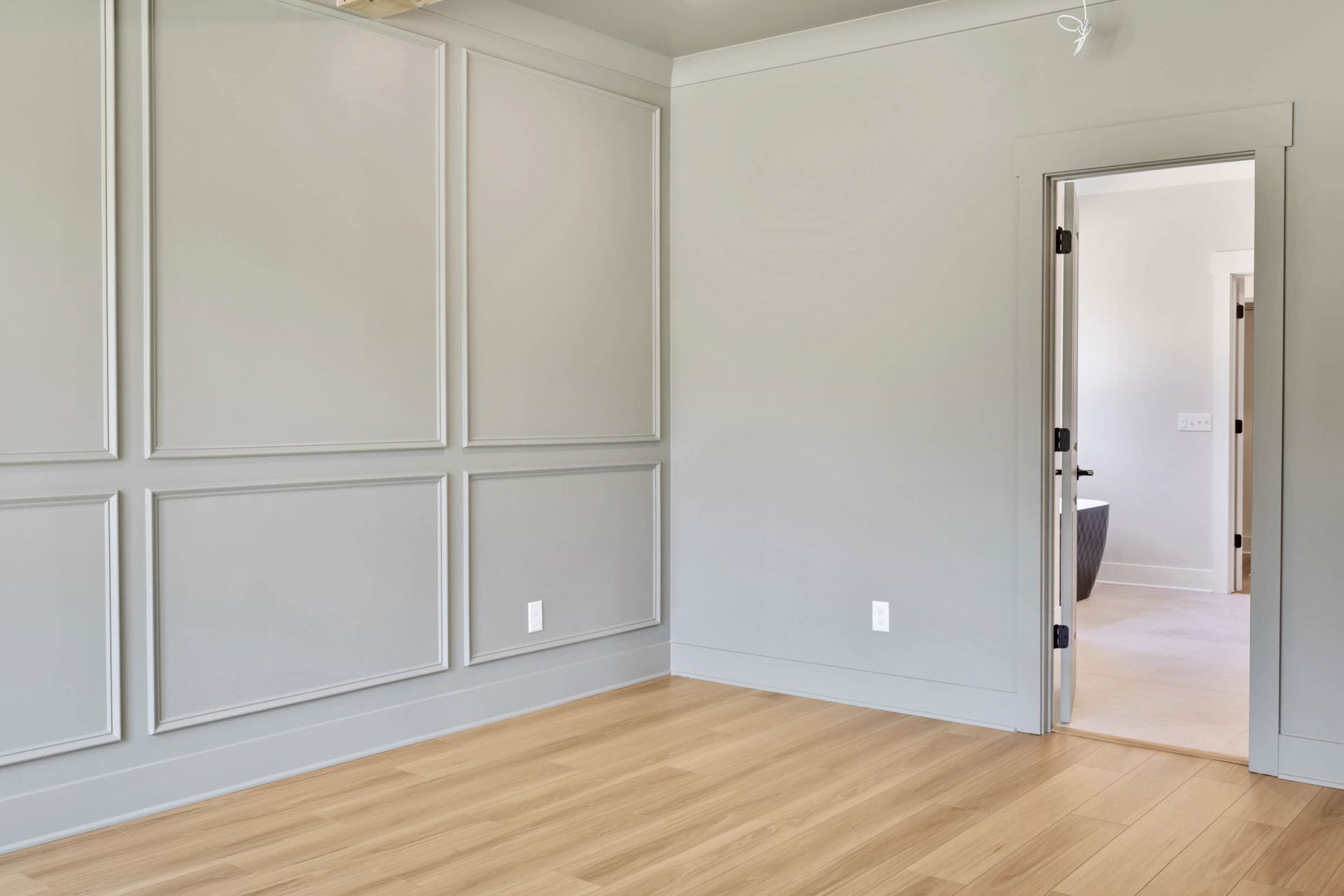 An empty room with gray walls and wooden floors and a door leading to a bathroom.