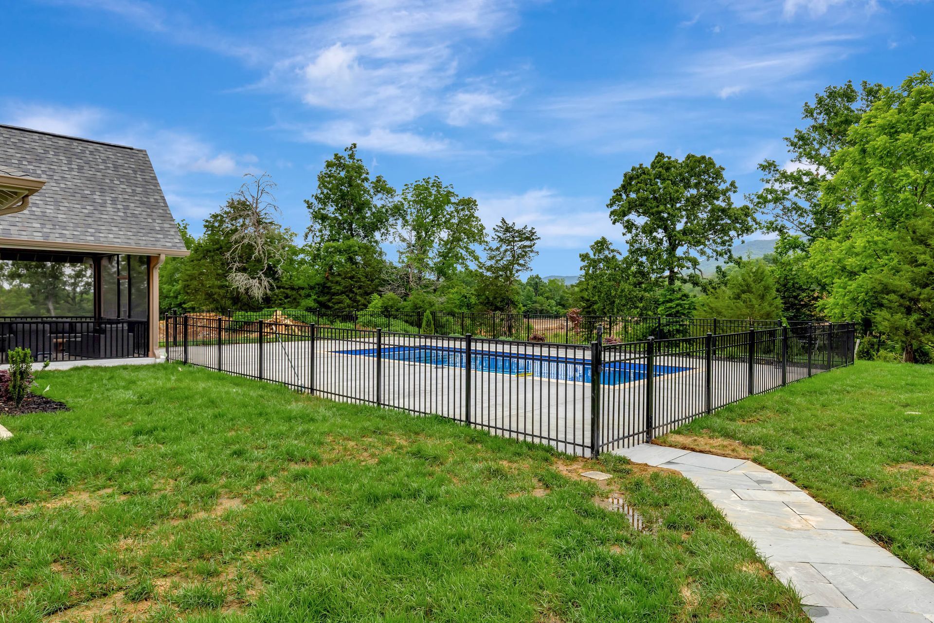There is a swimming pool behind a fence in the backyard of a house.