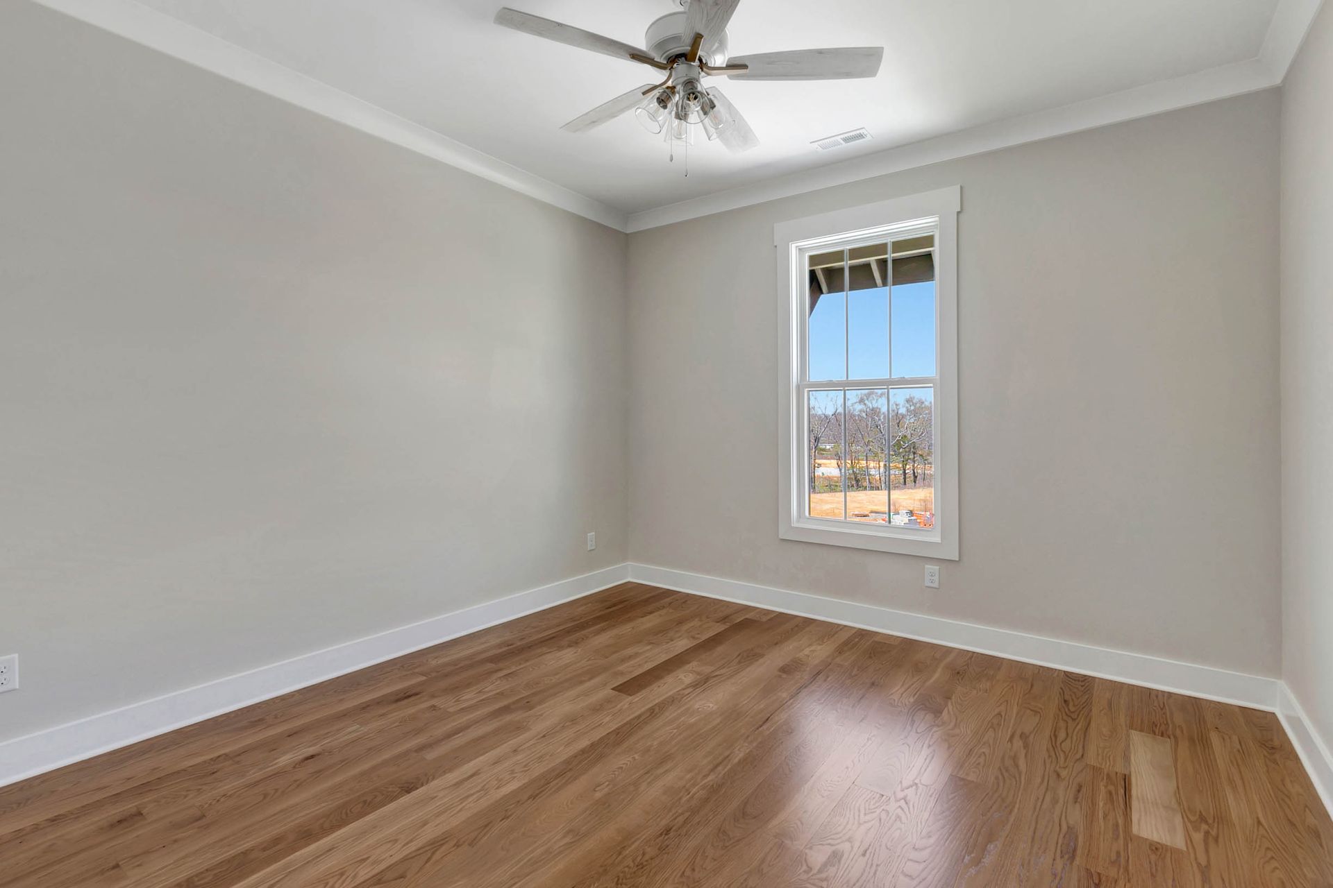 An empty bedroom with hardwood floors and a ceiling fan.