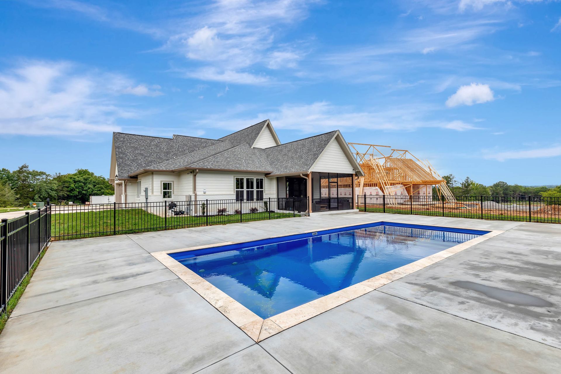 A house under construction with a large swimming pool in front of it.