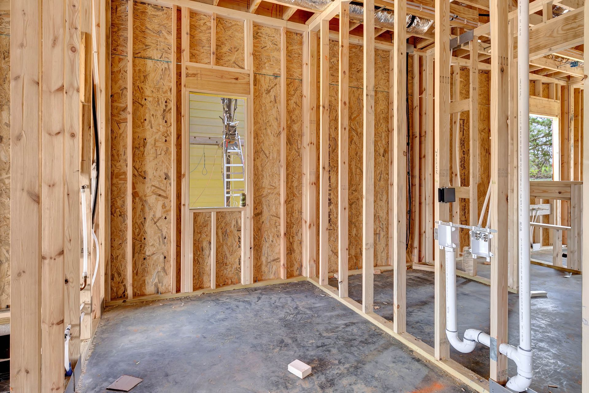 A room in a house under construction with wooden beams and pipes.