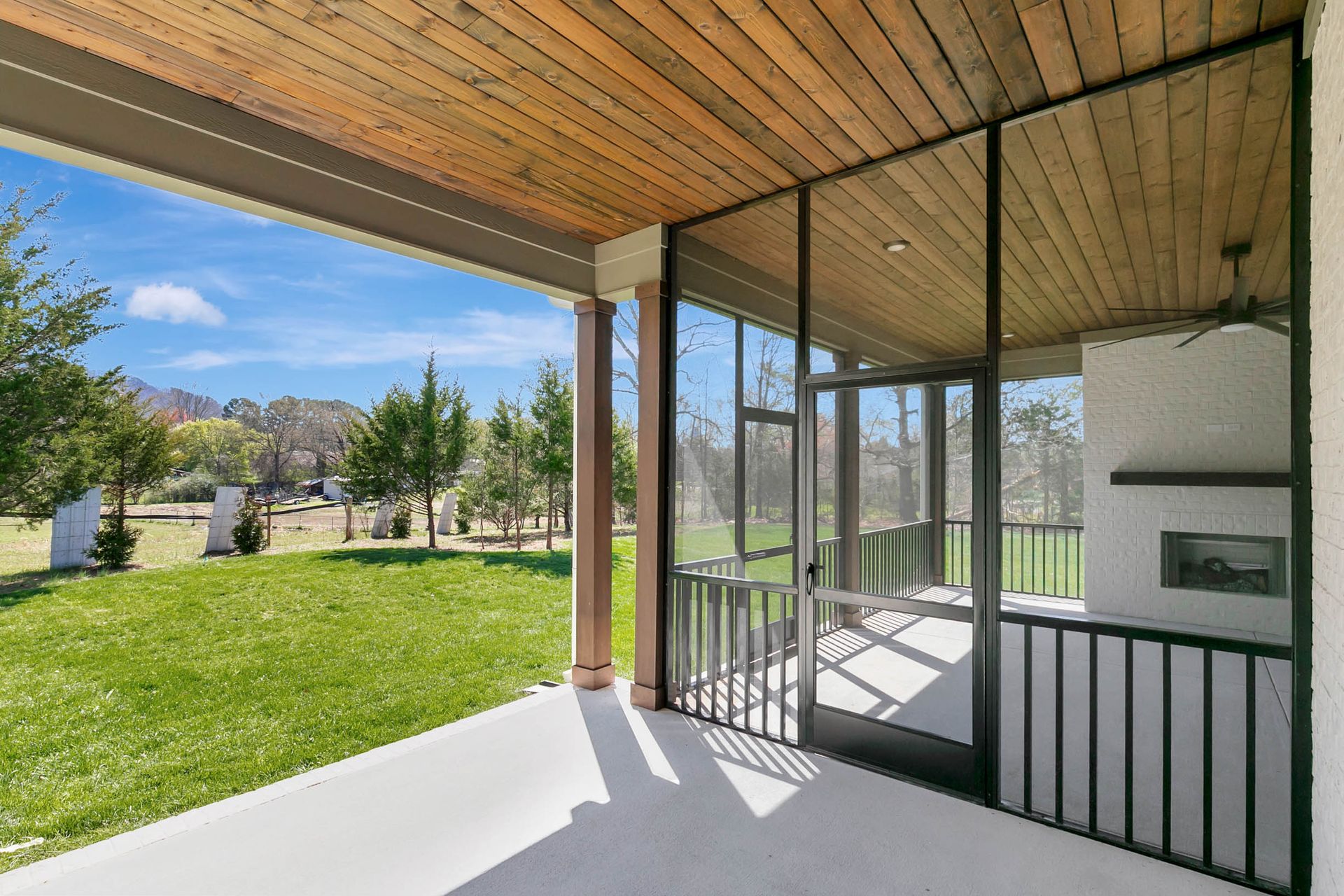 A screened in porch with a view of a lush green field.