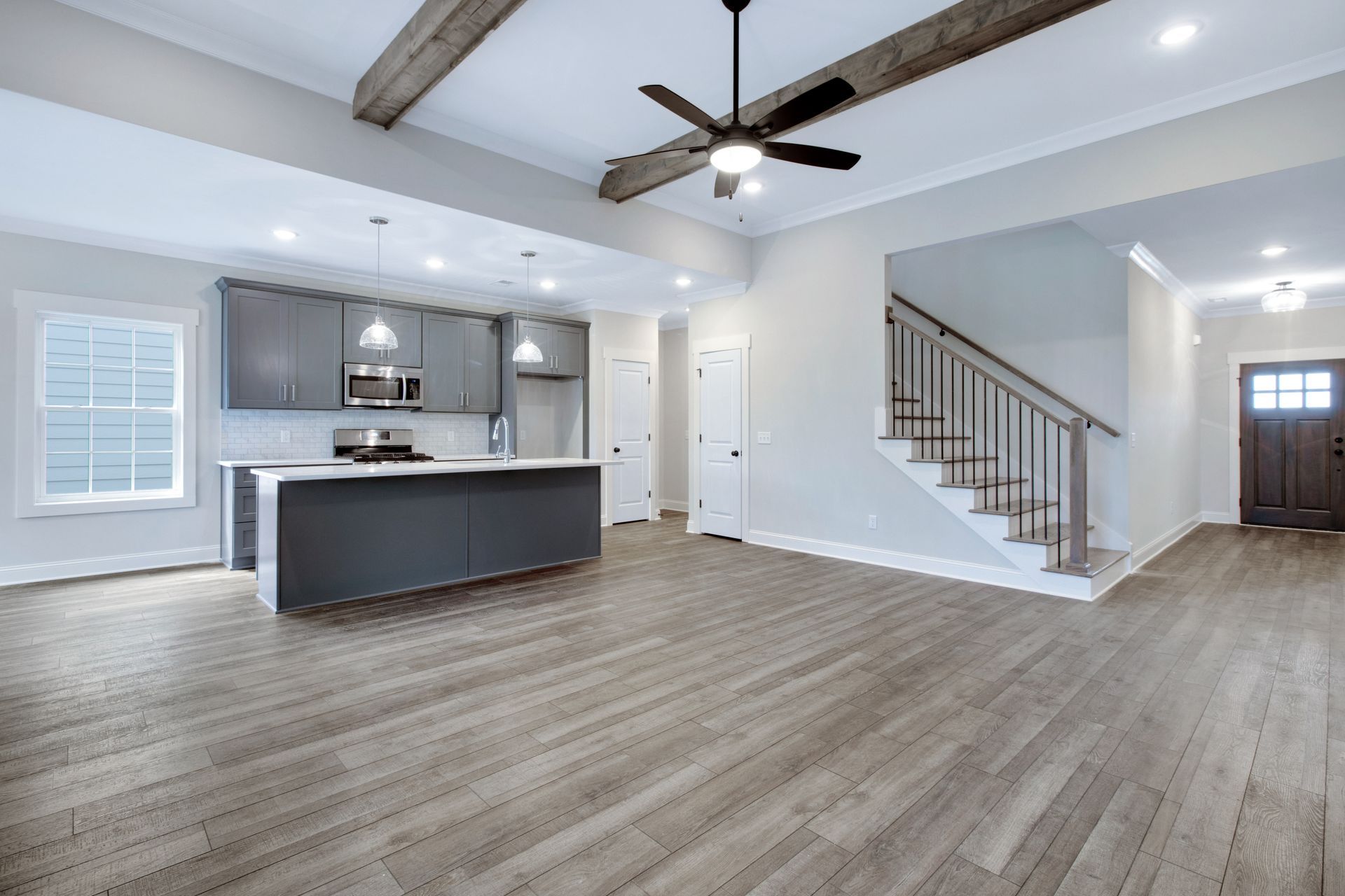 A kitchen and living room in a house with hardwood floors and a ceiling fan.
