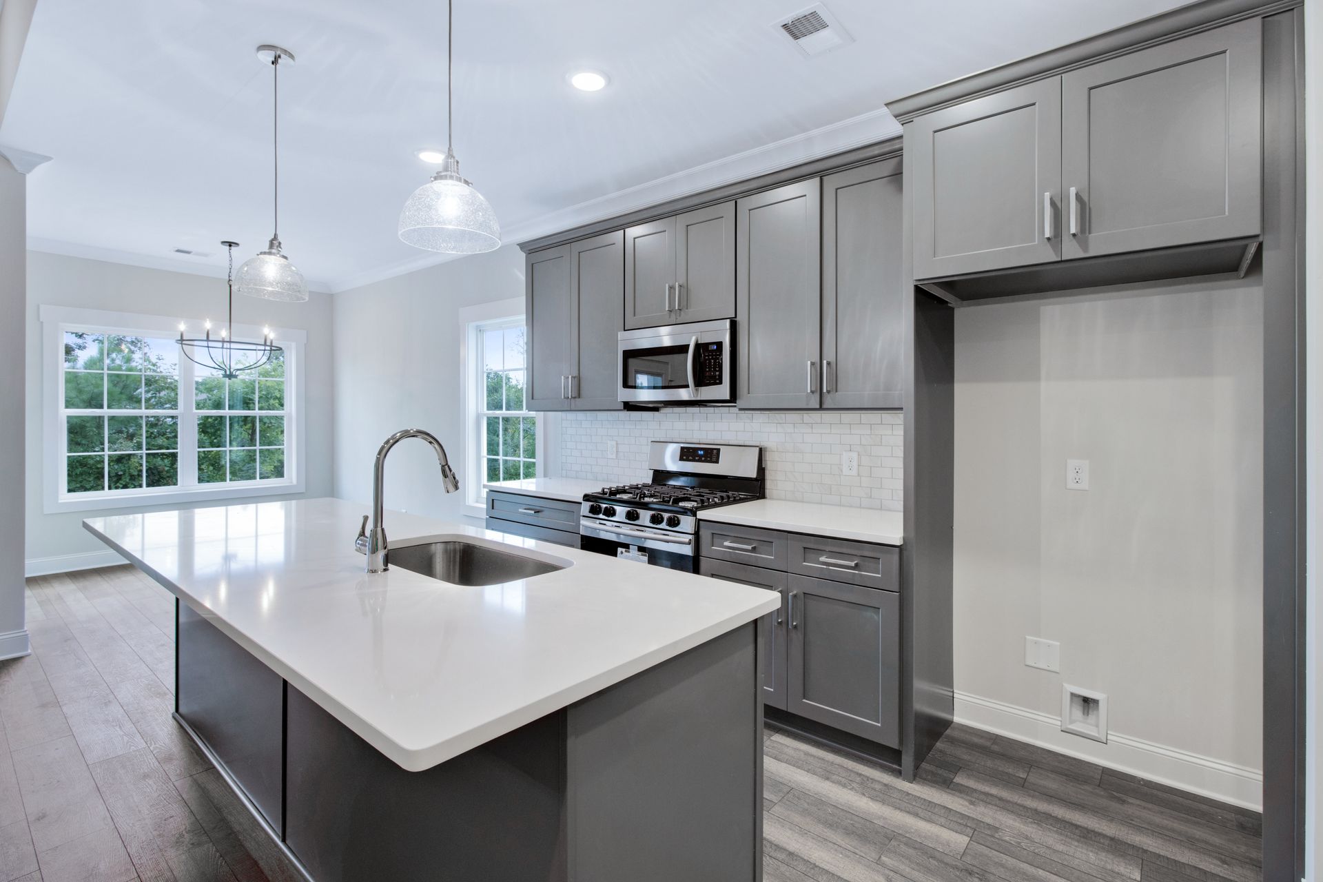 a kitchen with gray cabinets , white counter tops , a sink and a stove .